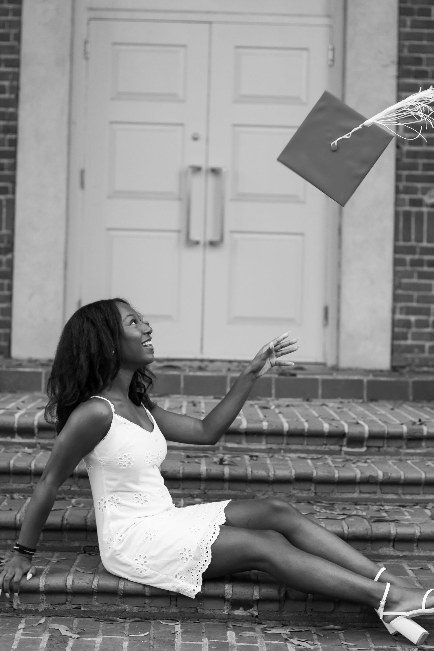 Graduation photo shoot showing graduate in white dress reclining on brick steps.