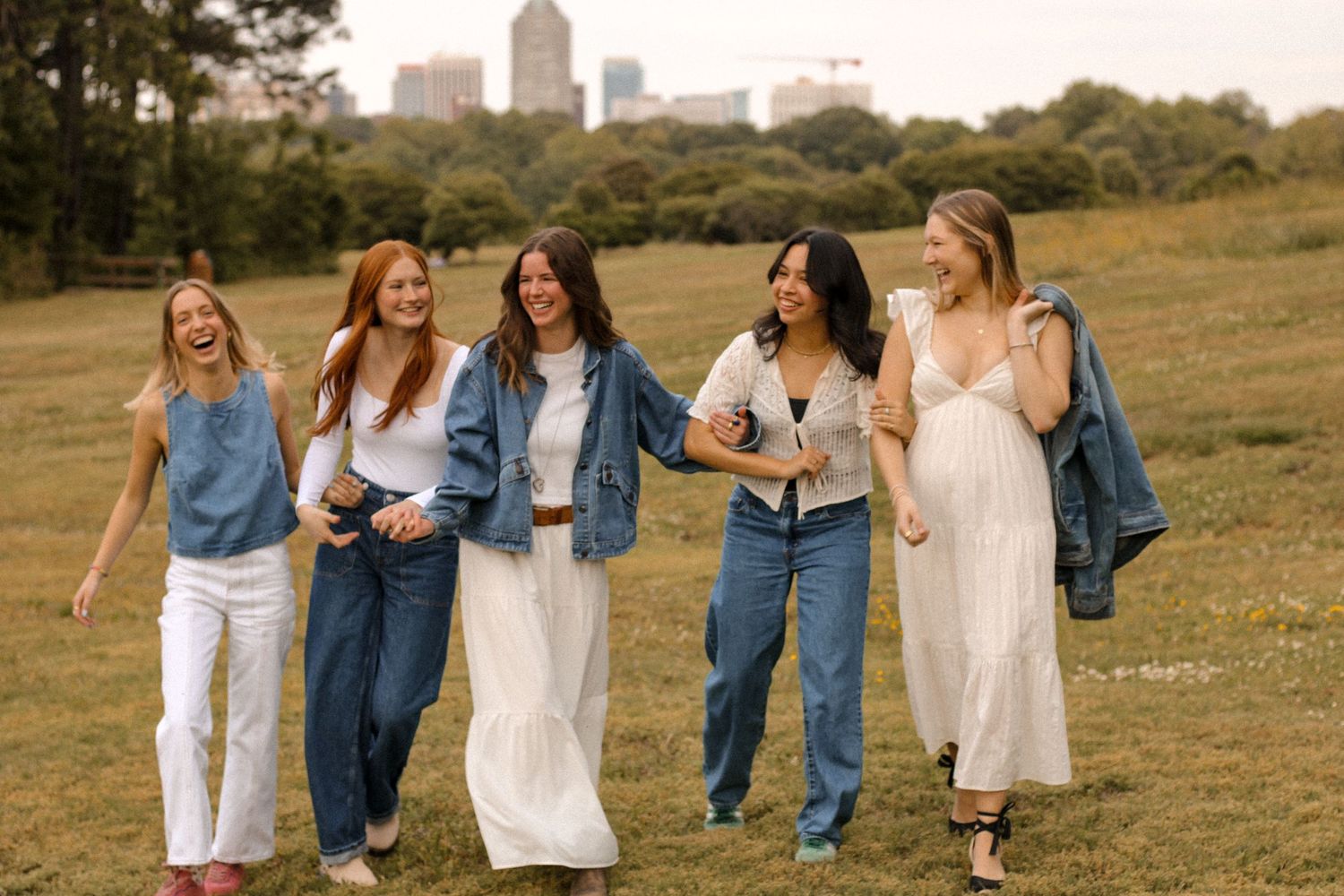 Friends walking together and laughing in casual outfits with urban skyline in background.