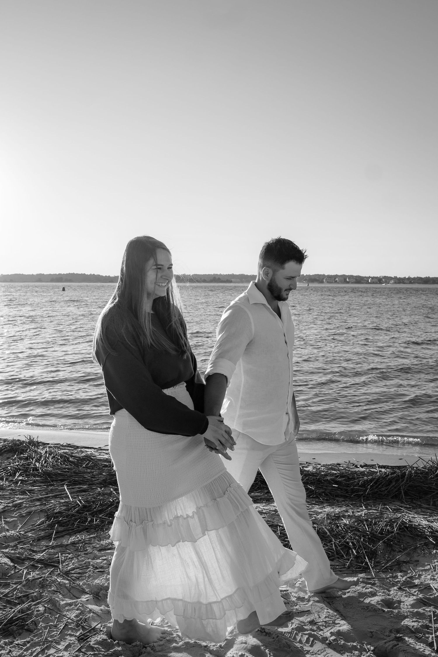 Black and white photo of couple sitting by ocean at sunset.