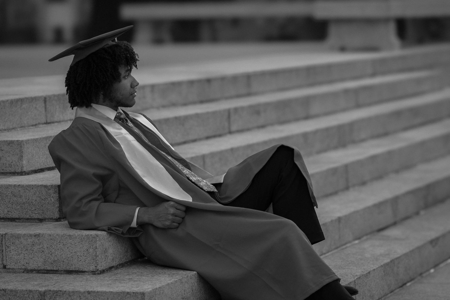Graduate in formal attire reclines on concrete steps during photo session.