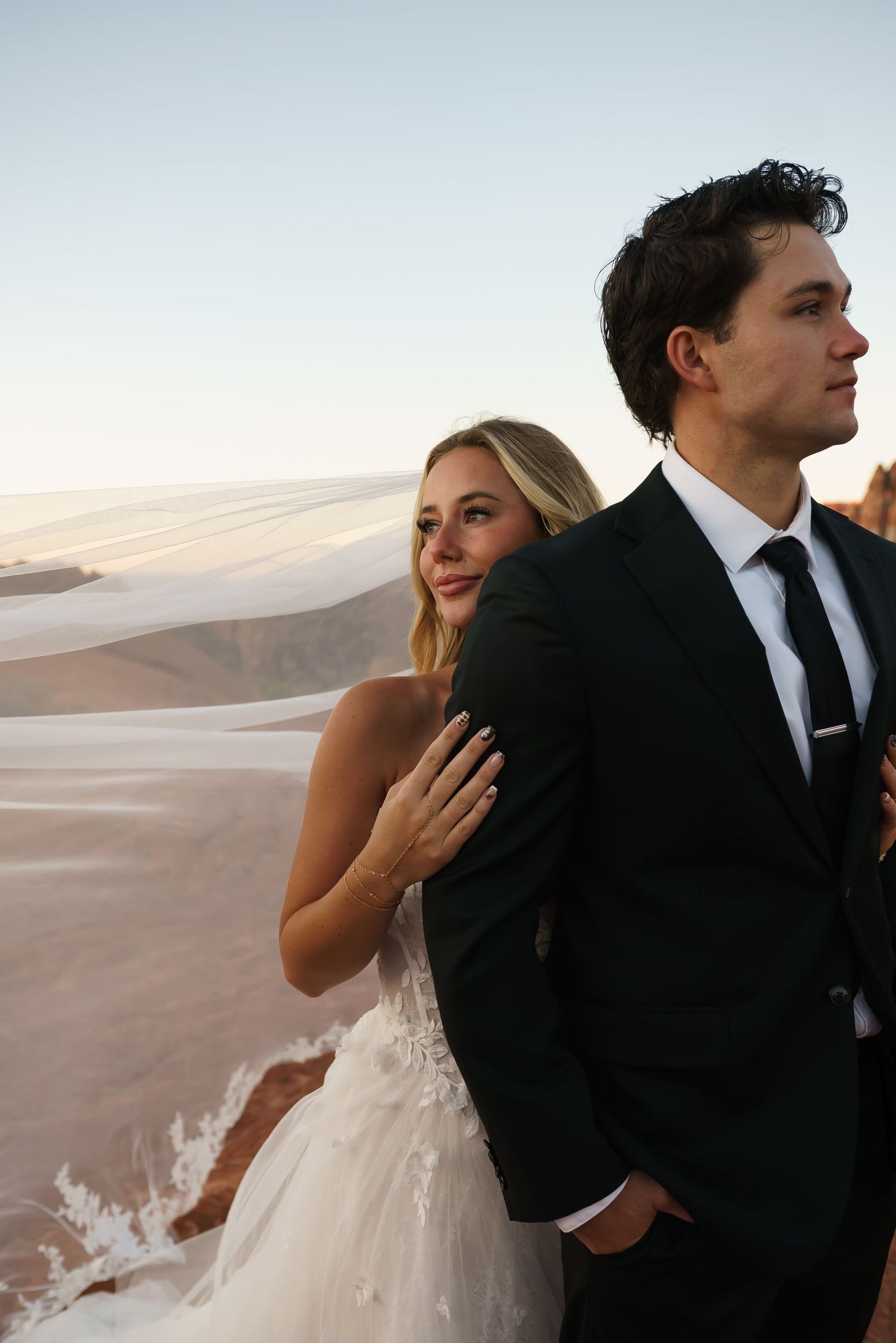 Couple in wedding attire posing dramatically against desert sand dunes.