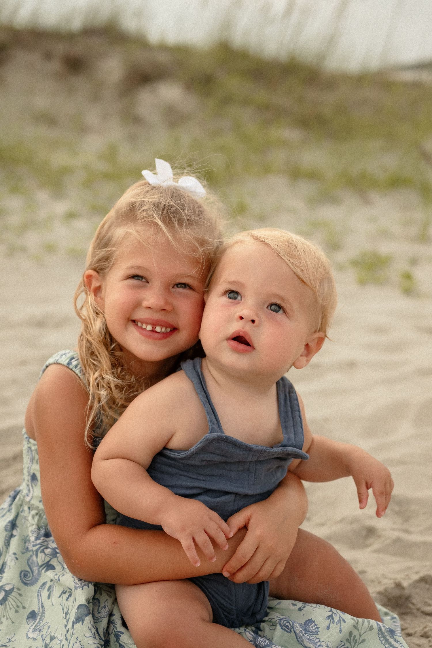 Two children share sweet embraces while playing together on a sandy beach.