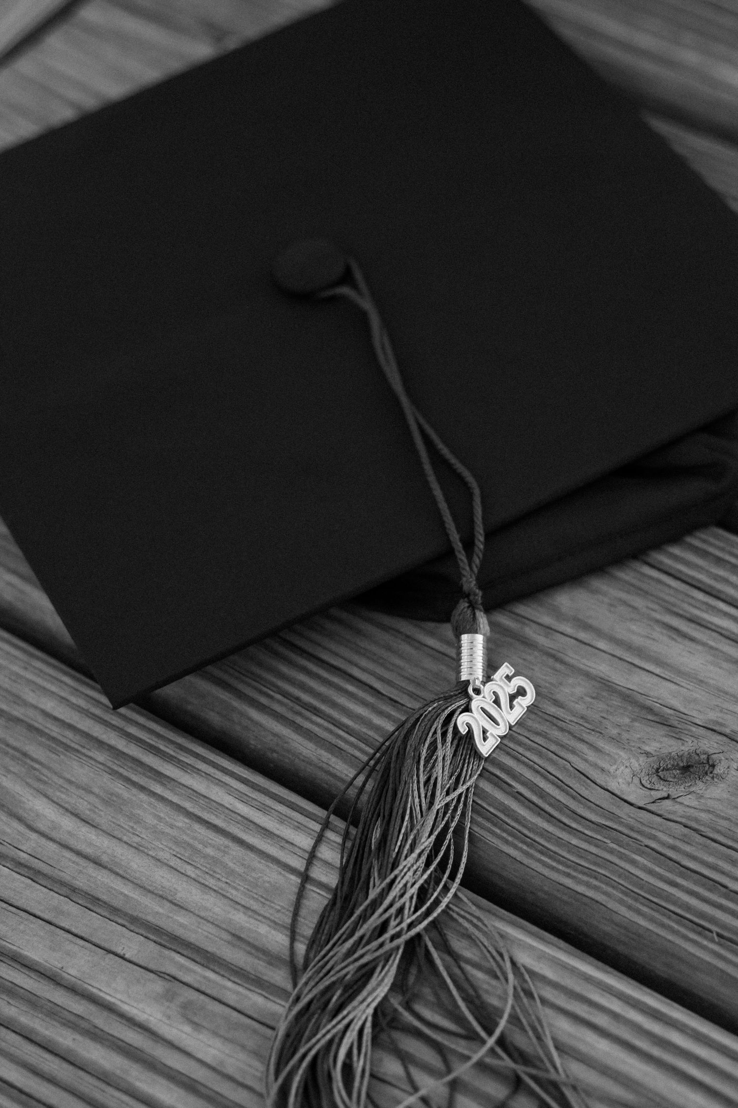 Close-up of black graduation cap with 2023 tassel on wooden deck.