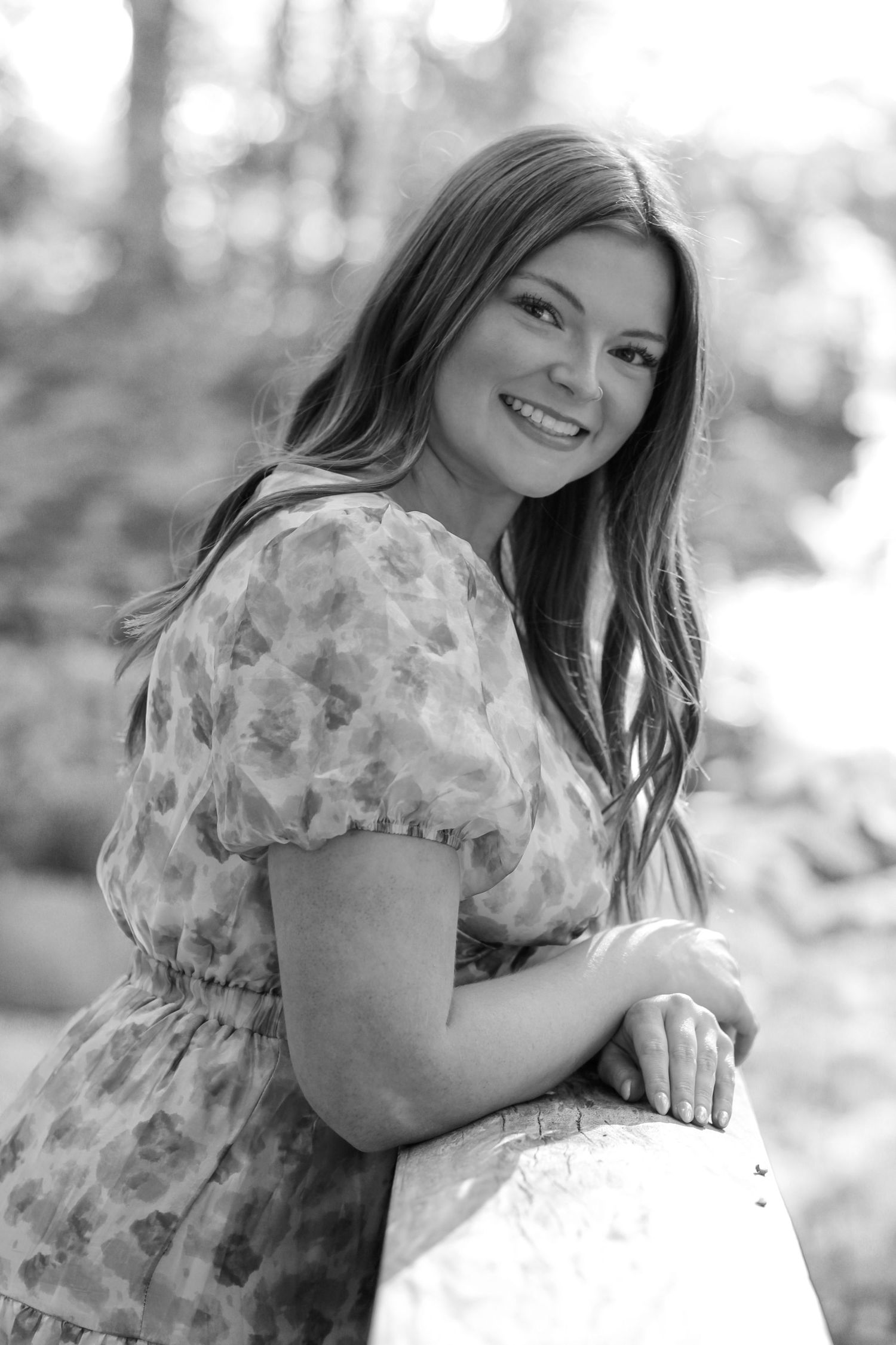 Black and white portrait of graduate in floral dress leaning against railing.