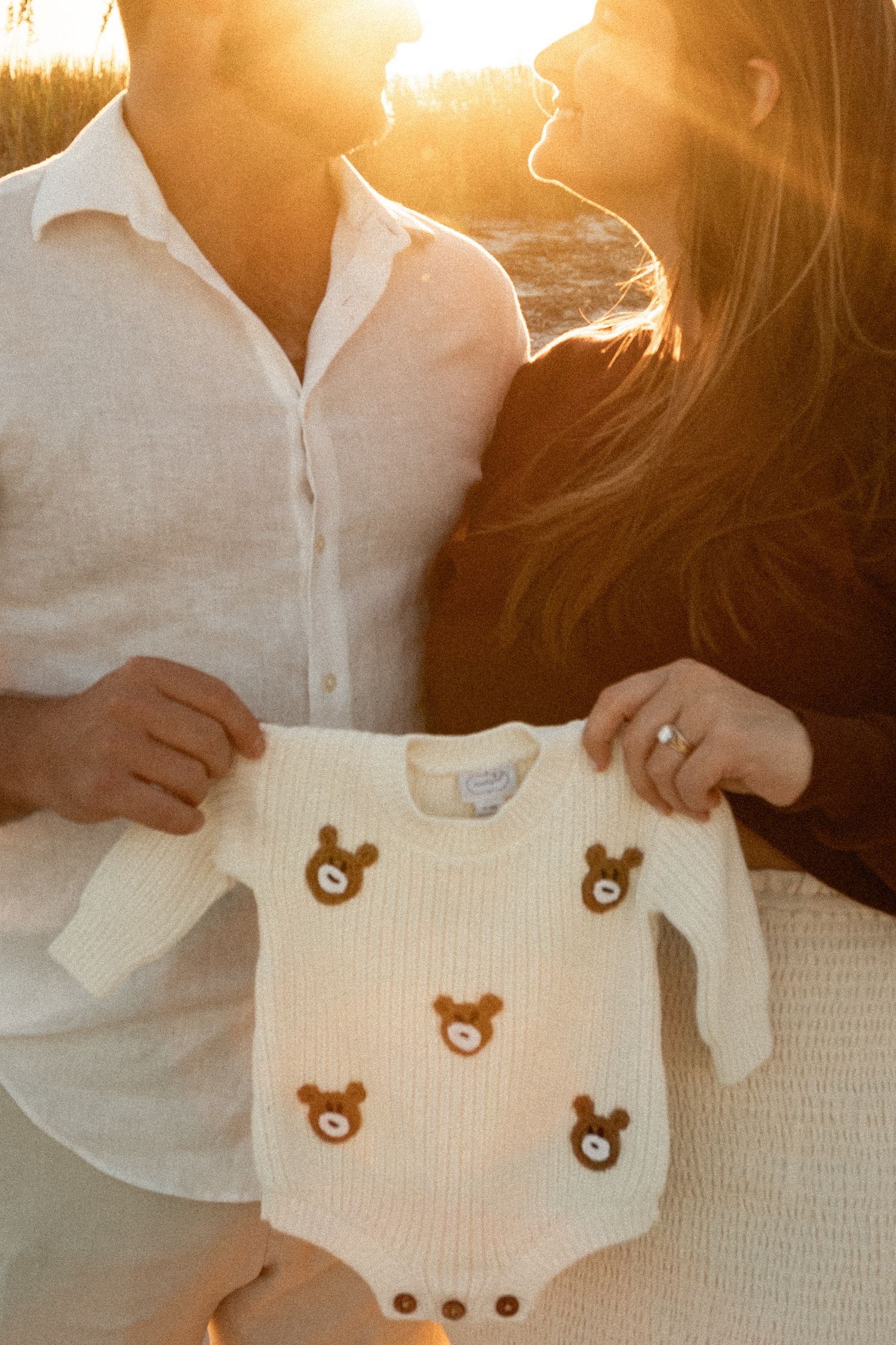 Sunset photo showing a white baby onesie with teddy bear prints being held up.