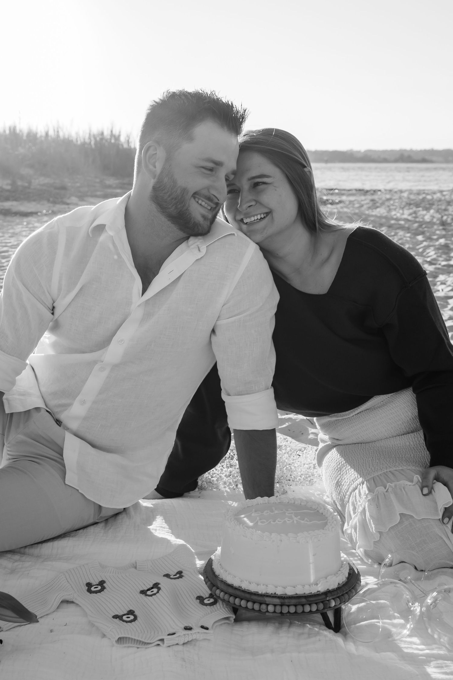 Black and white photo of couple with cake during beach picnic.