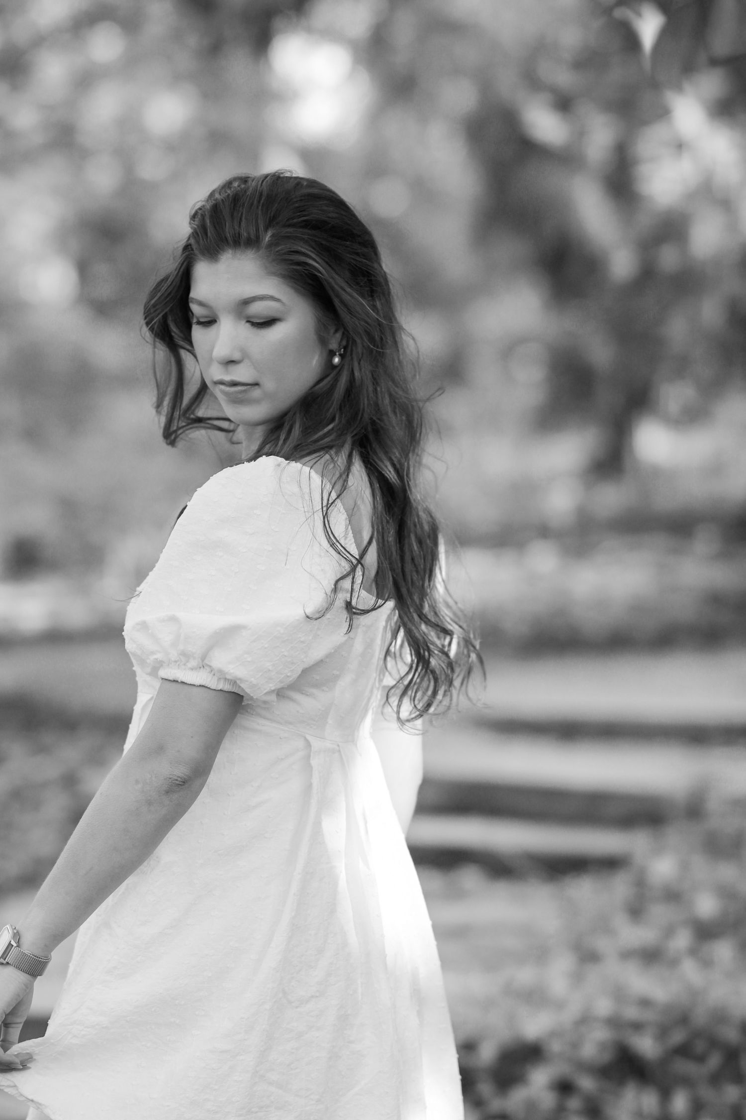 Black and white portrait of person in white dress with puff sleeves looking over shoulder.