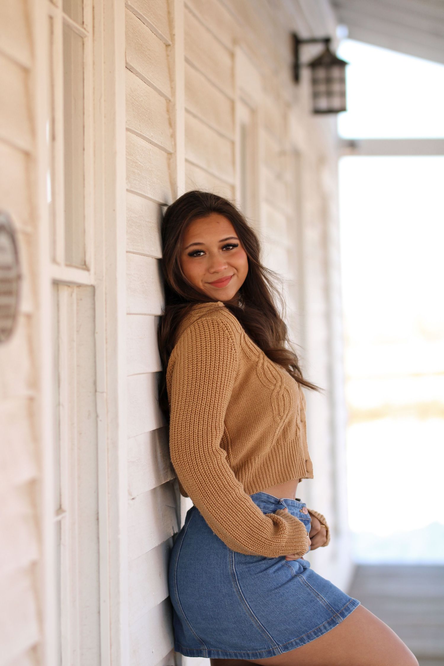 Fashion portrait in a bright hallway wearing a tan sweater and denim shorts.