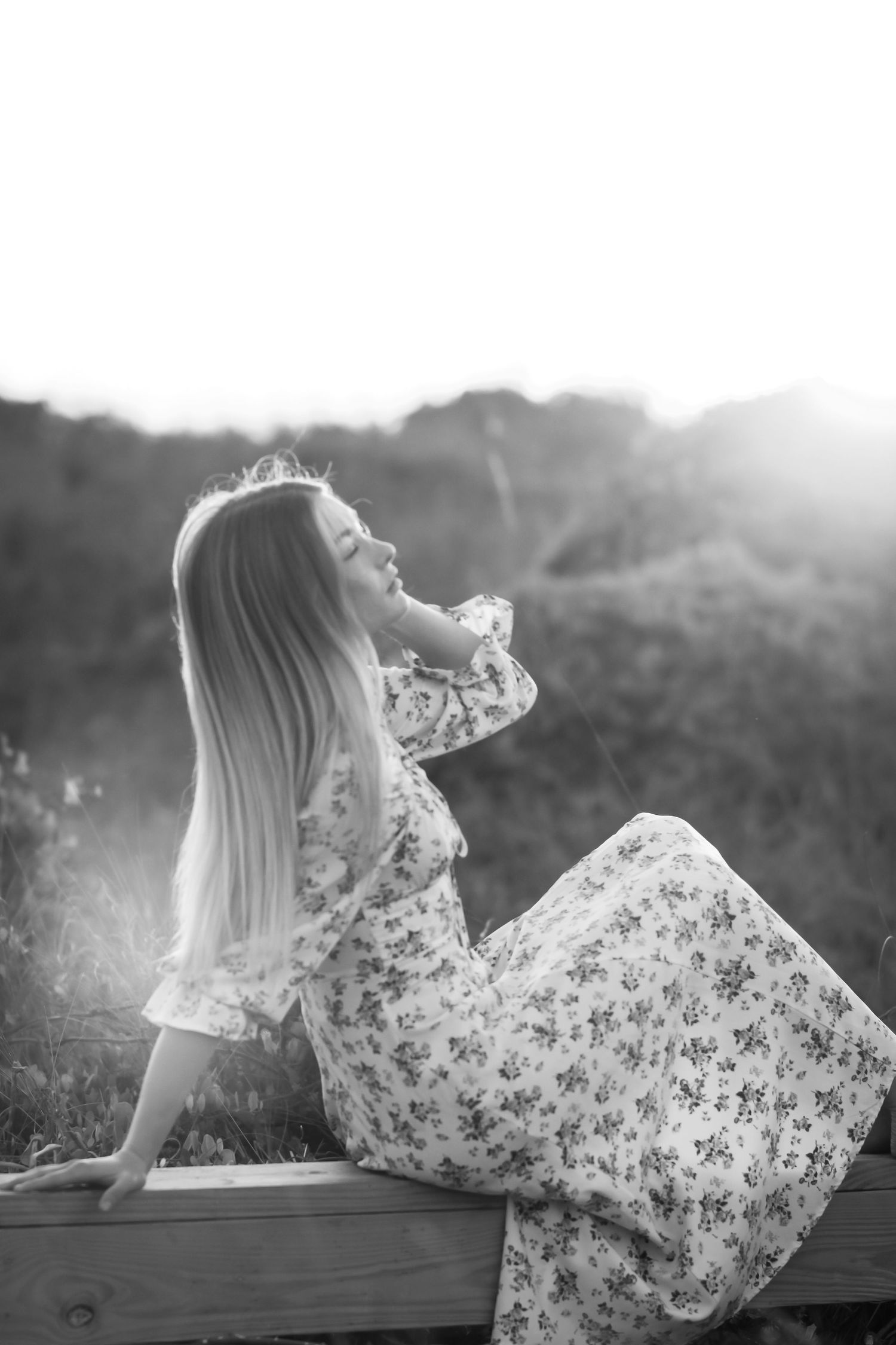 Artistic photos of someone in a floral dress lounging on a wooden railing at sunset.