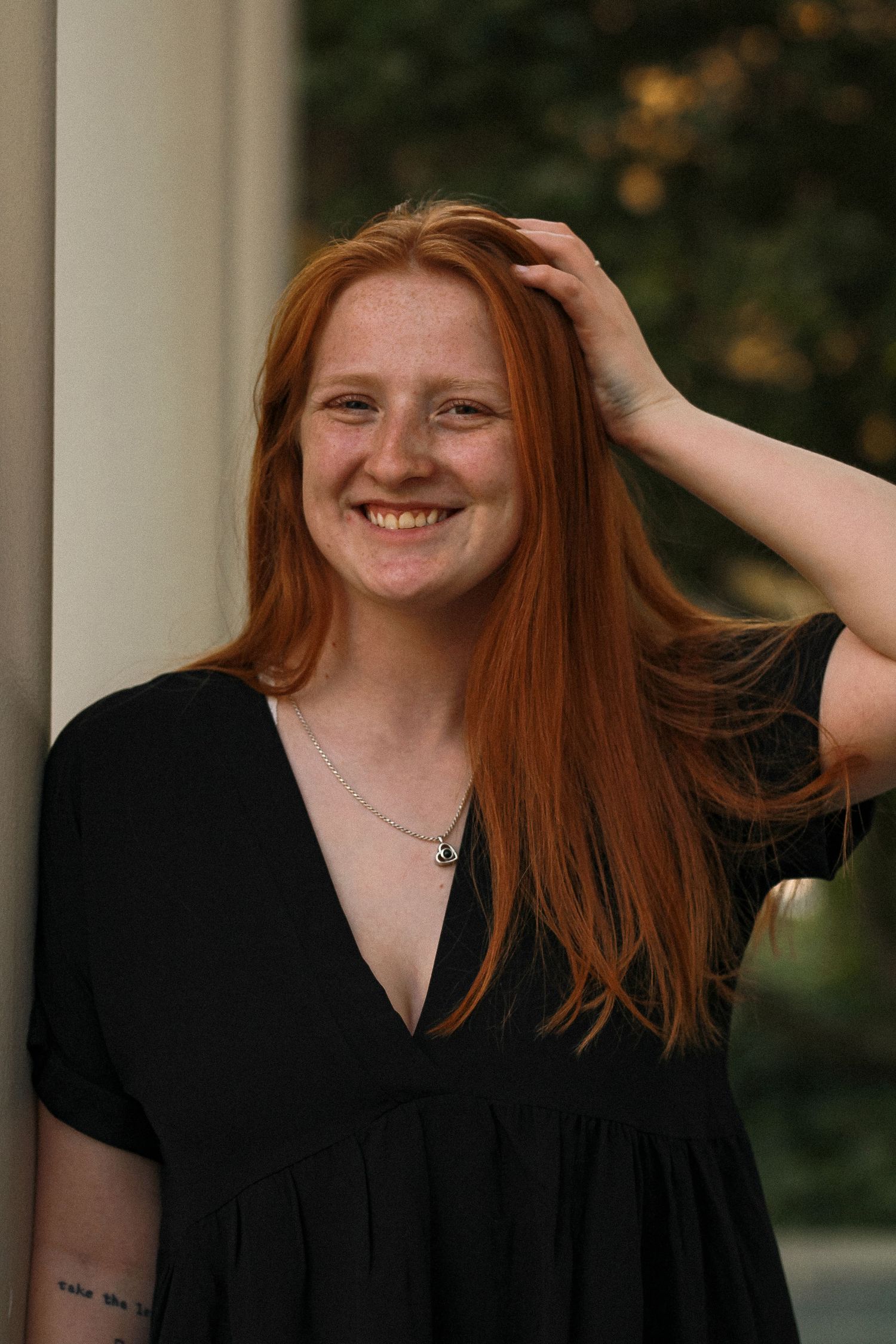 Person in black dress playing with hair against white pillars at sunset.