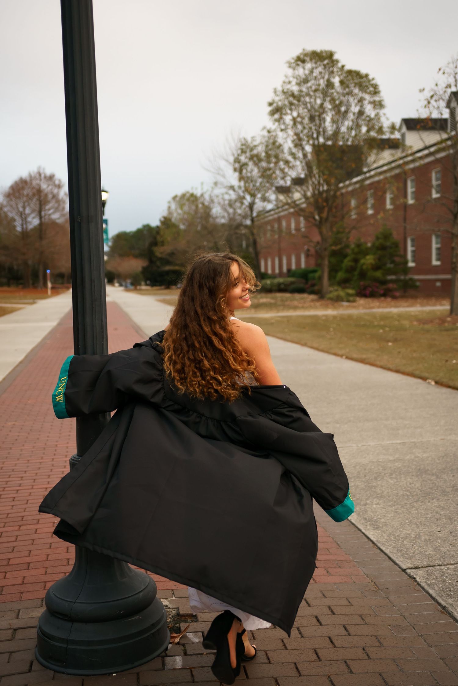 Graduate in academic gown leaning against lamp post on brick pathway.