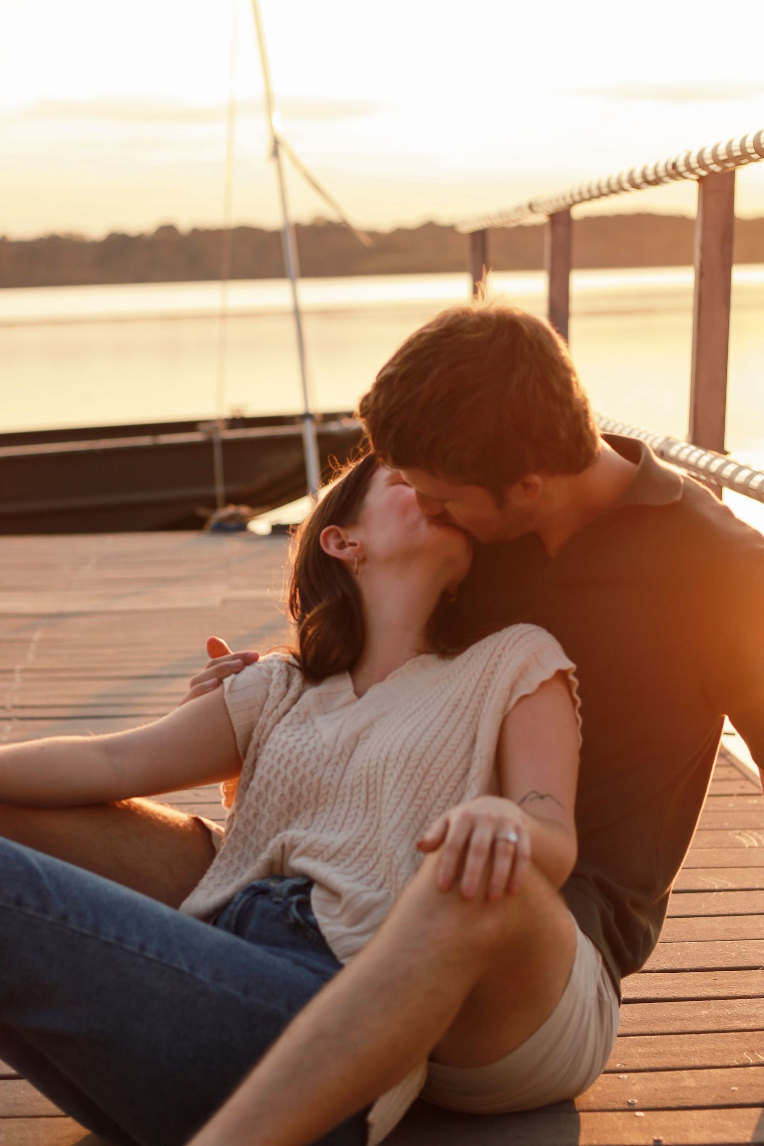 A couple embraces on a wooden dock during a golden sunset over the water.