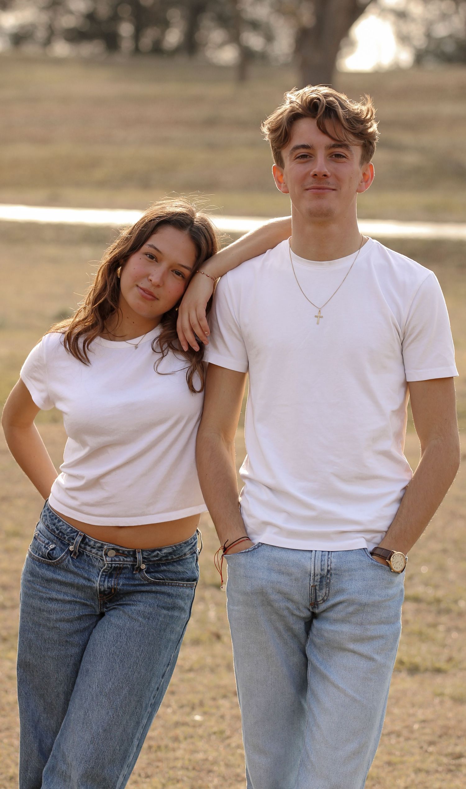 Young couple in white t-shirts and jeans pose together outdoors in warm sunlight.