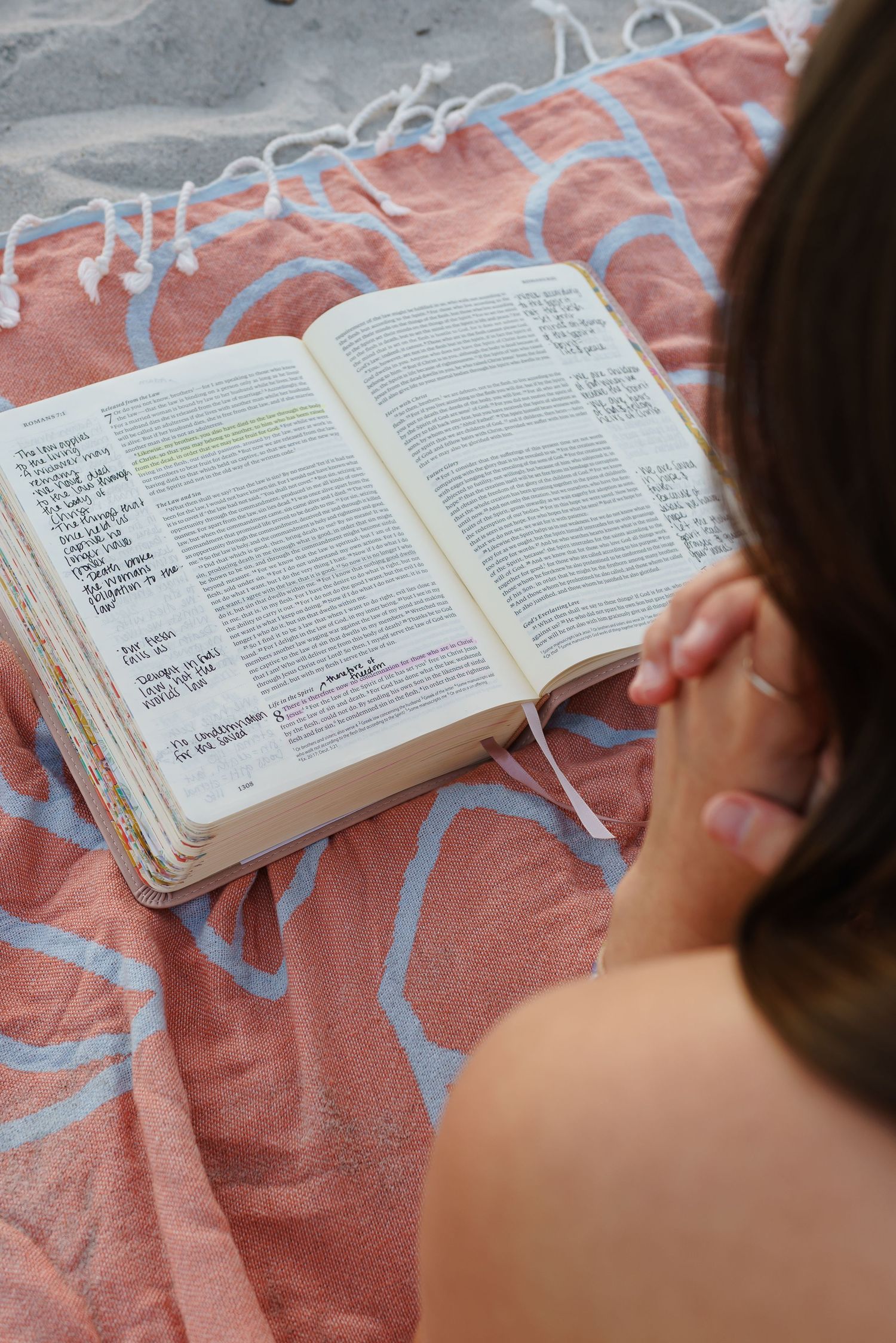 Woman reading an annotated Bible on a coral patterned beach towel outdoors.