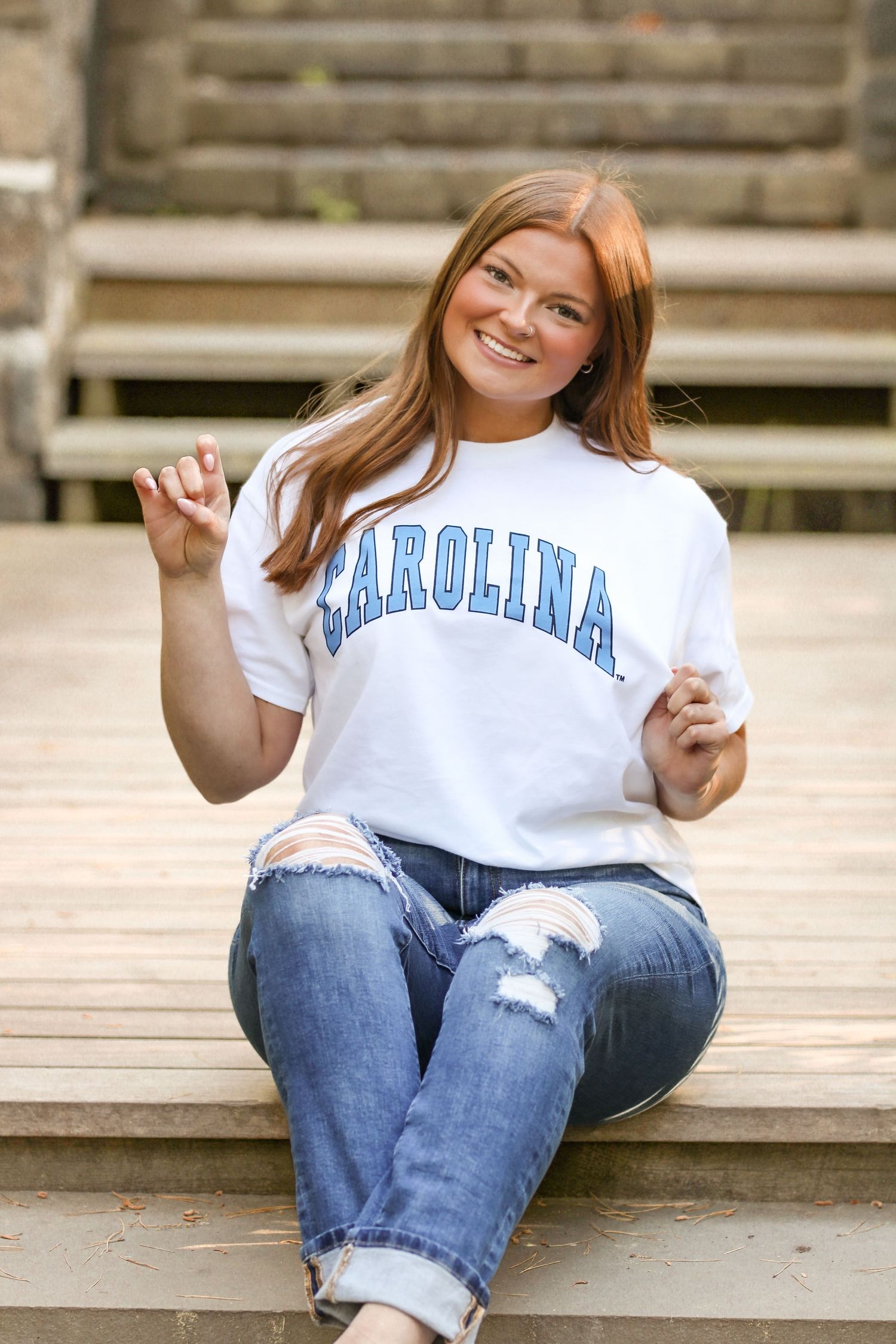 Casual portrait series showing person in university t-shirt and jeans on wooden deck.