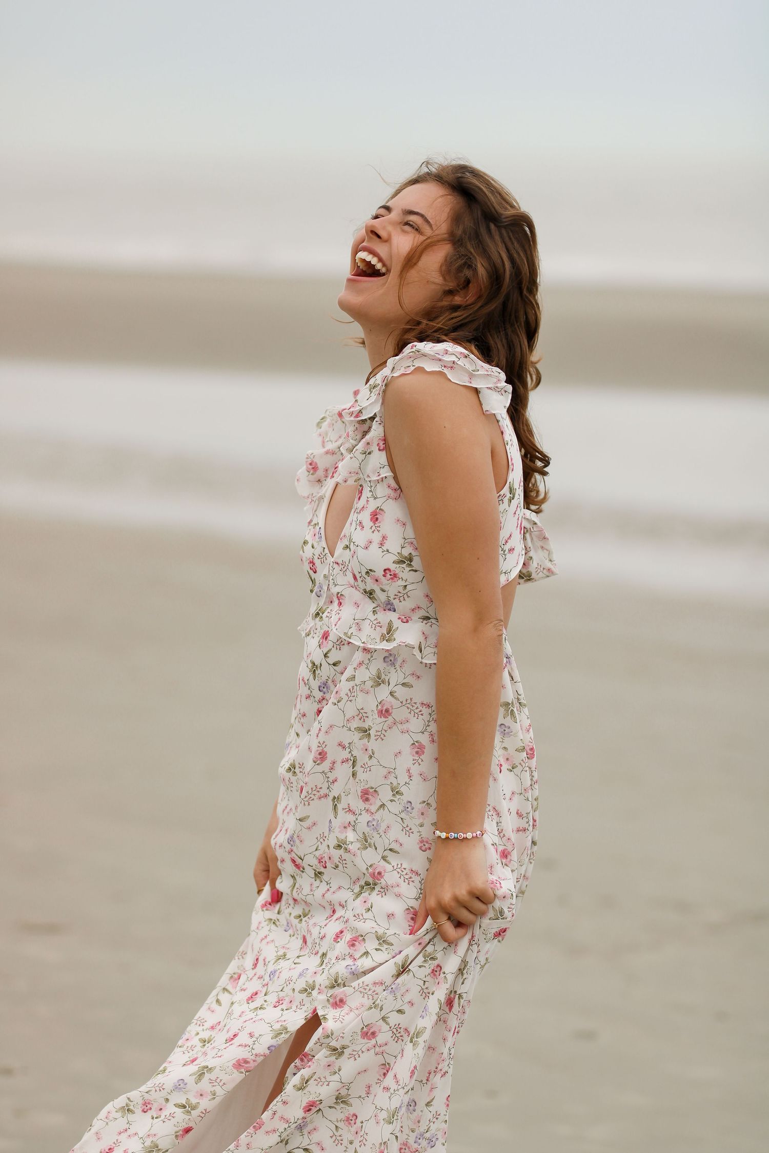 A candid laughing moment in a floral dress on the beach.