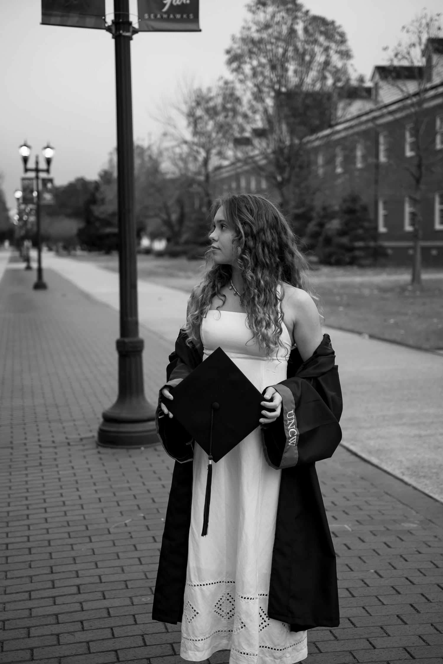 Black and white photo series of a graduate posing with their graduation gown on a brick walkway.