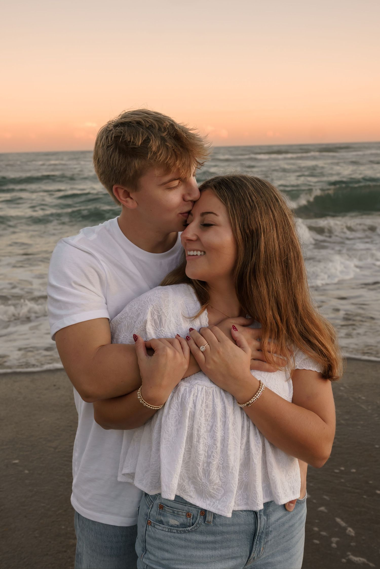 A tender moment shared between a couple on the beach at dusk.