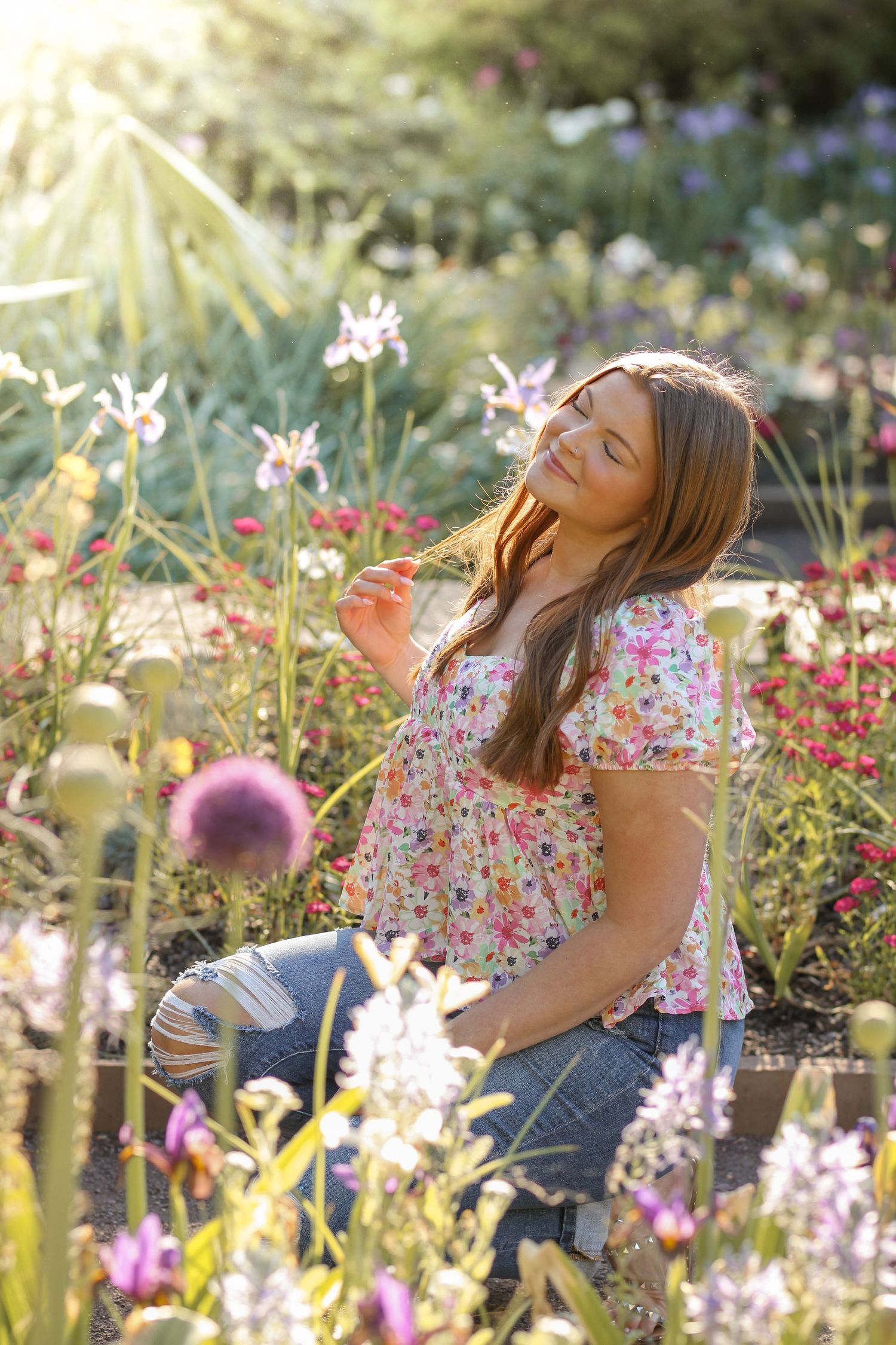 A person wearing a floral dress enjoys a sunny moment in a blooming garden.