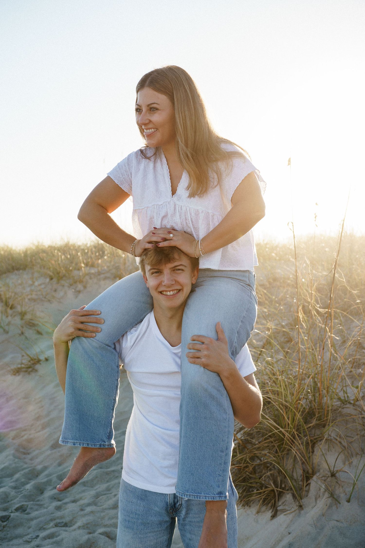 Joyful couple playing and laughing together on beach sand dunes in casual attire.