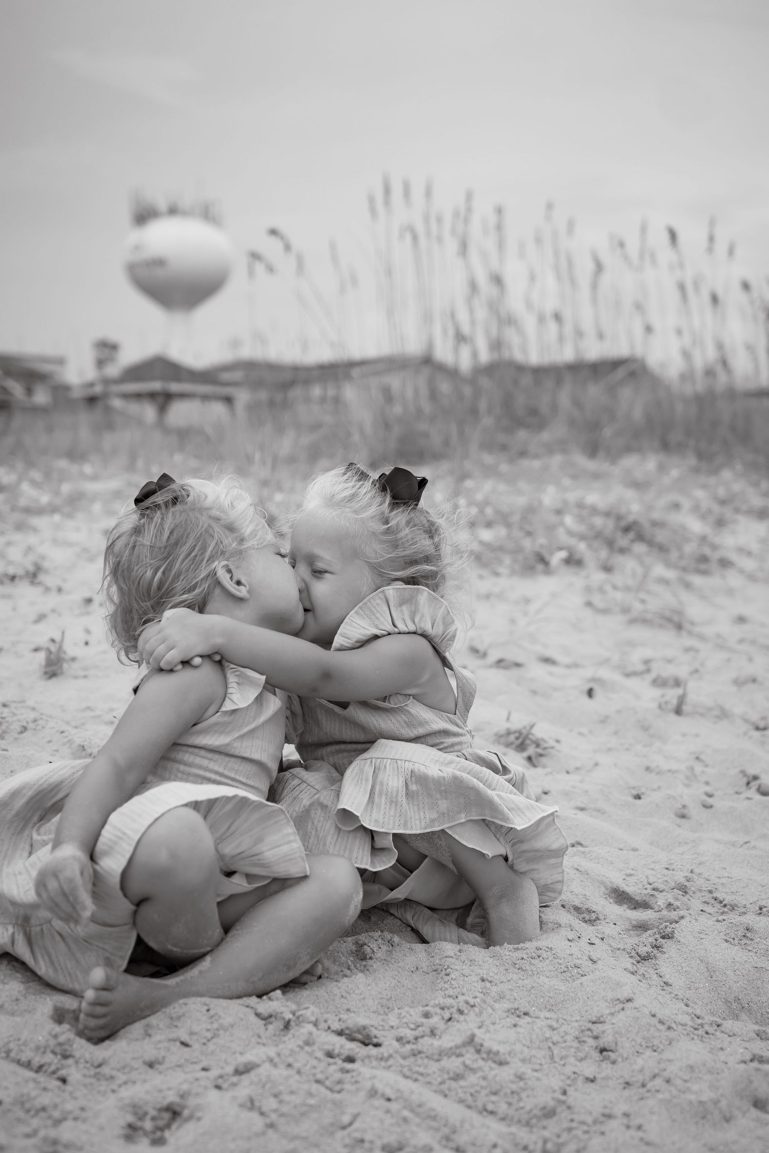 Black and white photo sequence of two children playing and rolling in beach sand.