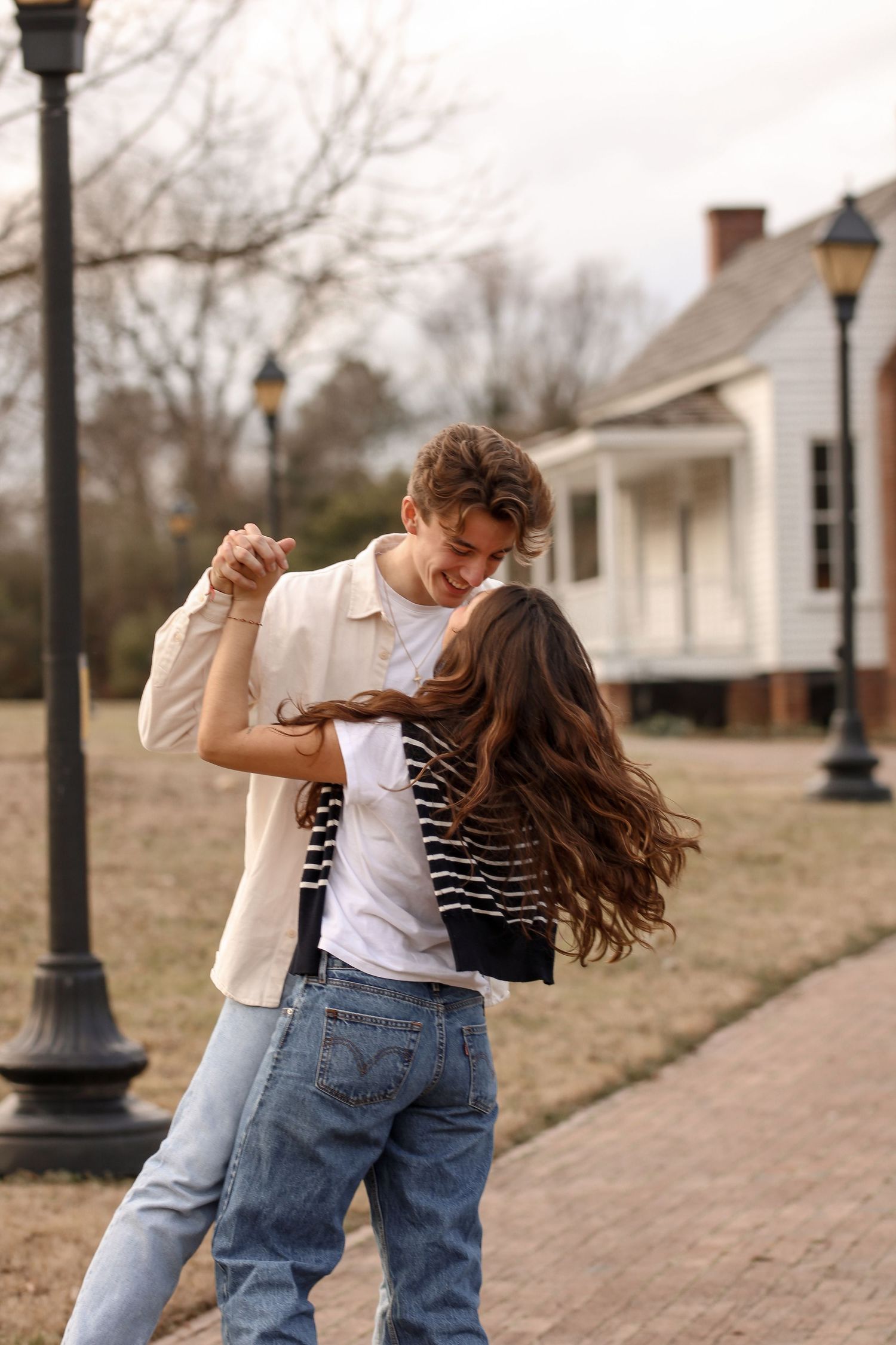 A playful dance scene on a brick pathway with vintage lampposts and houses in the background.