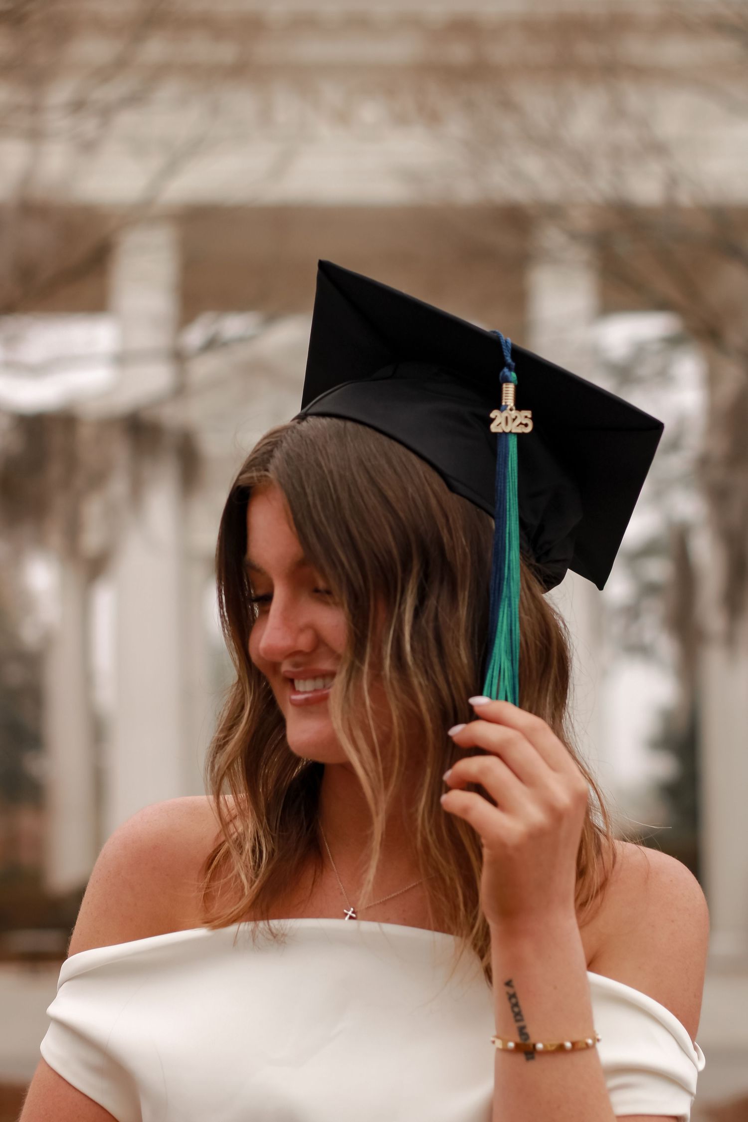 Graduate wearing mortarboard cap with green tassel and white dress smiles during celebration.
