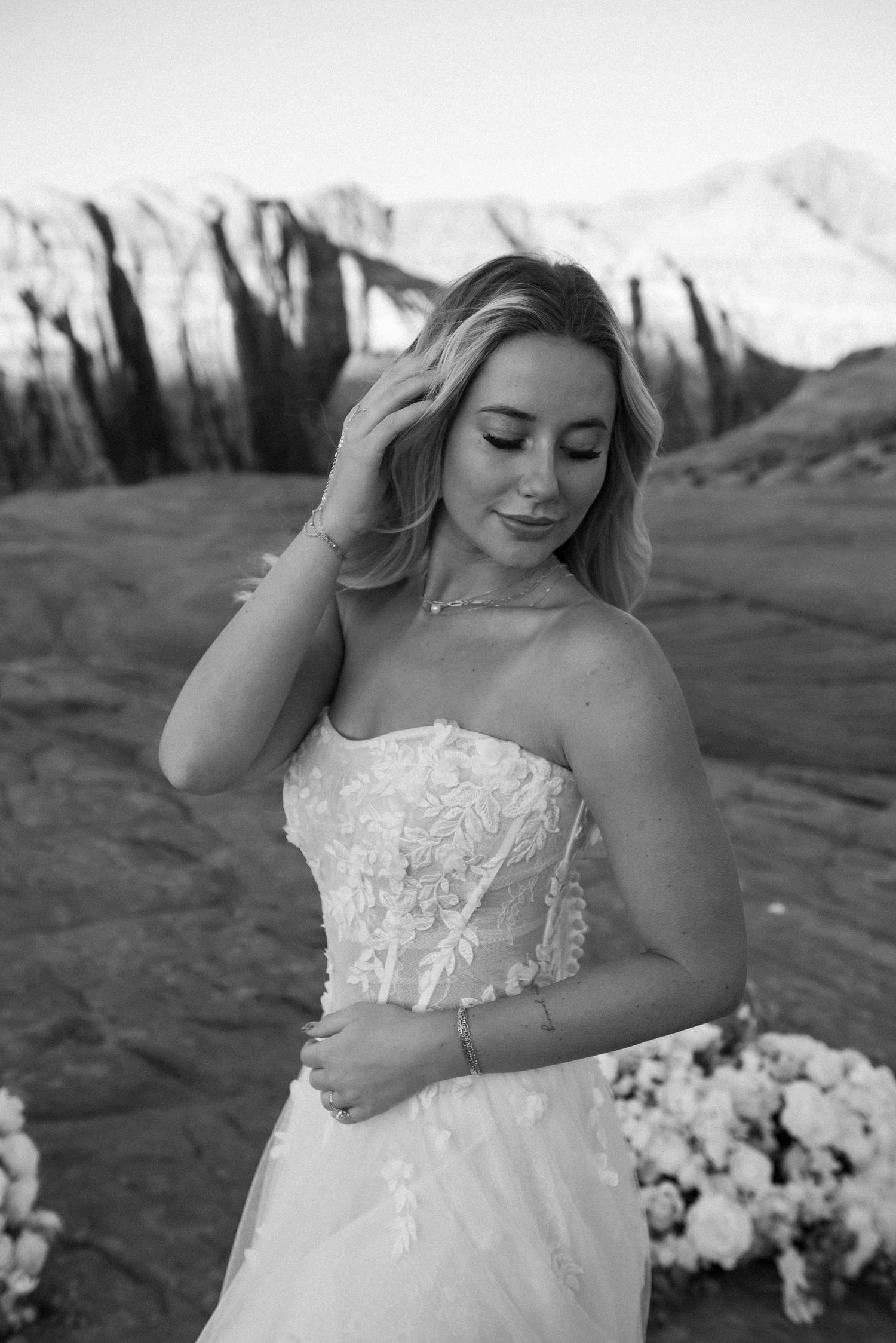 Black and white bridal portraits showcasing an elegant strapless wedding gown against desert cliffs.