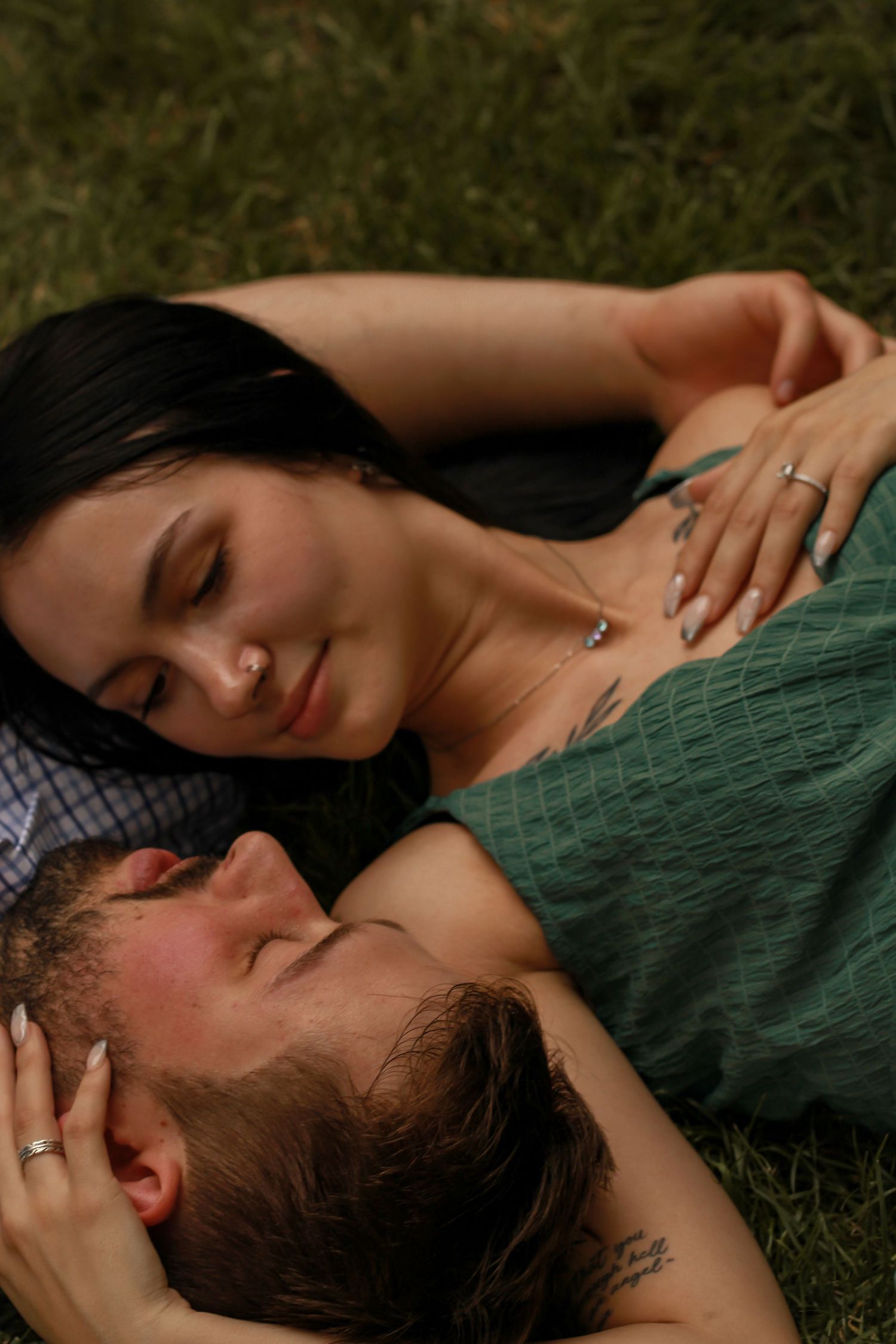 A couple lying together on grass sharing an intimate moment.