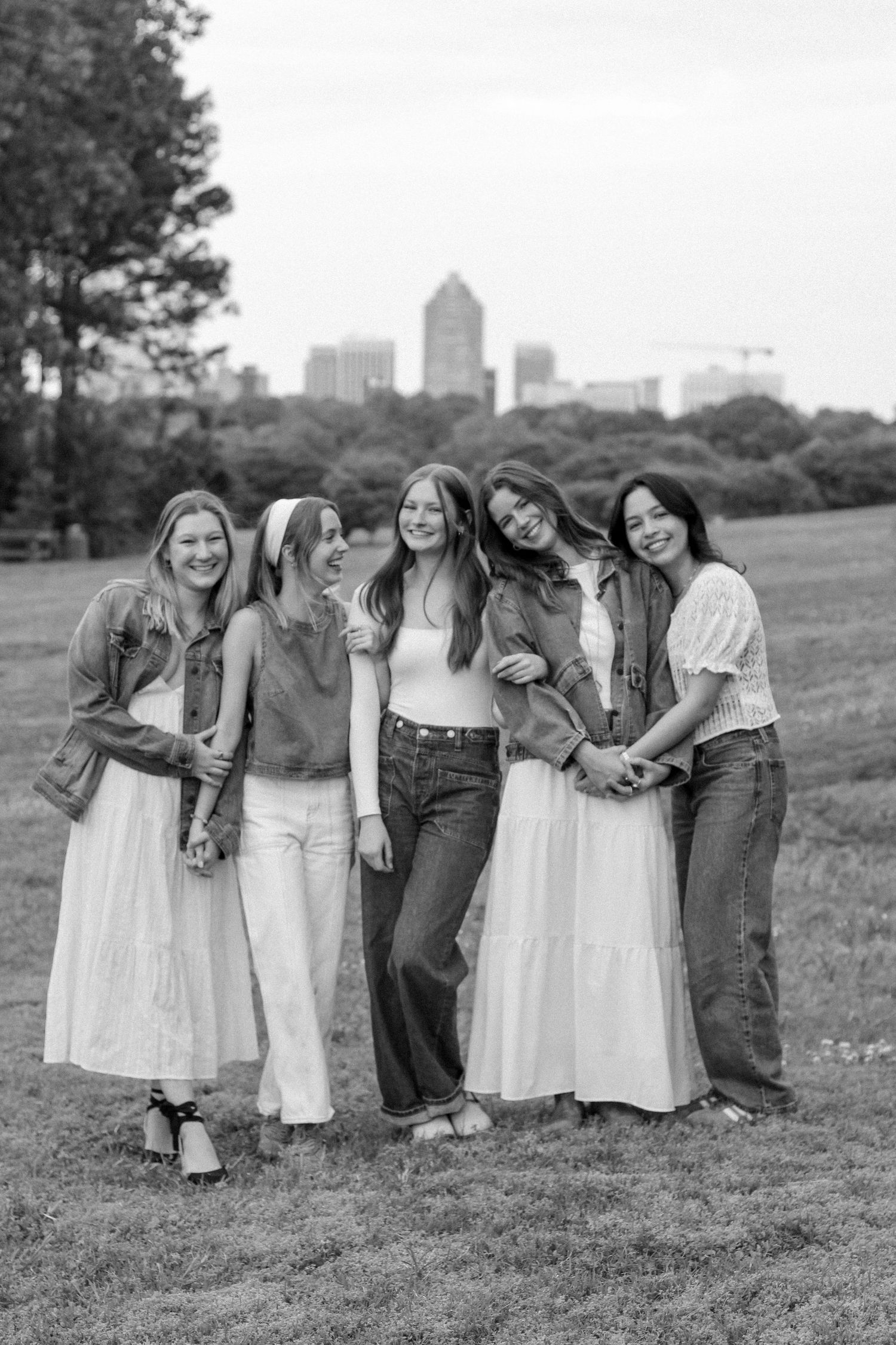 Group of friends in casual outfits laugh together outdoors with city buildings visible in background.