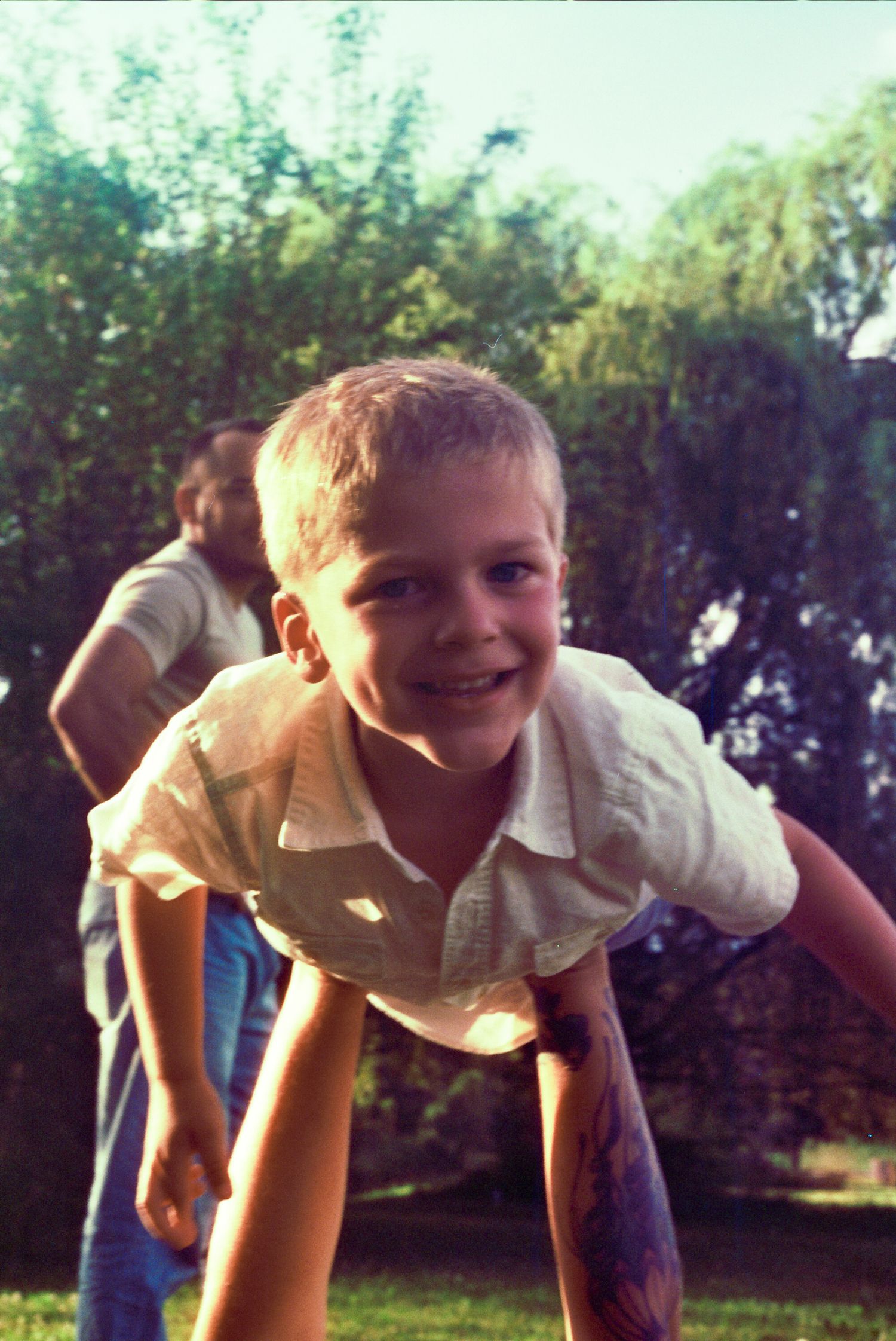 A playful child leans forward while being held up in a sequence of repeated photos outdoors on a sunny day.