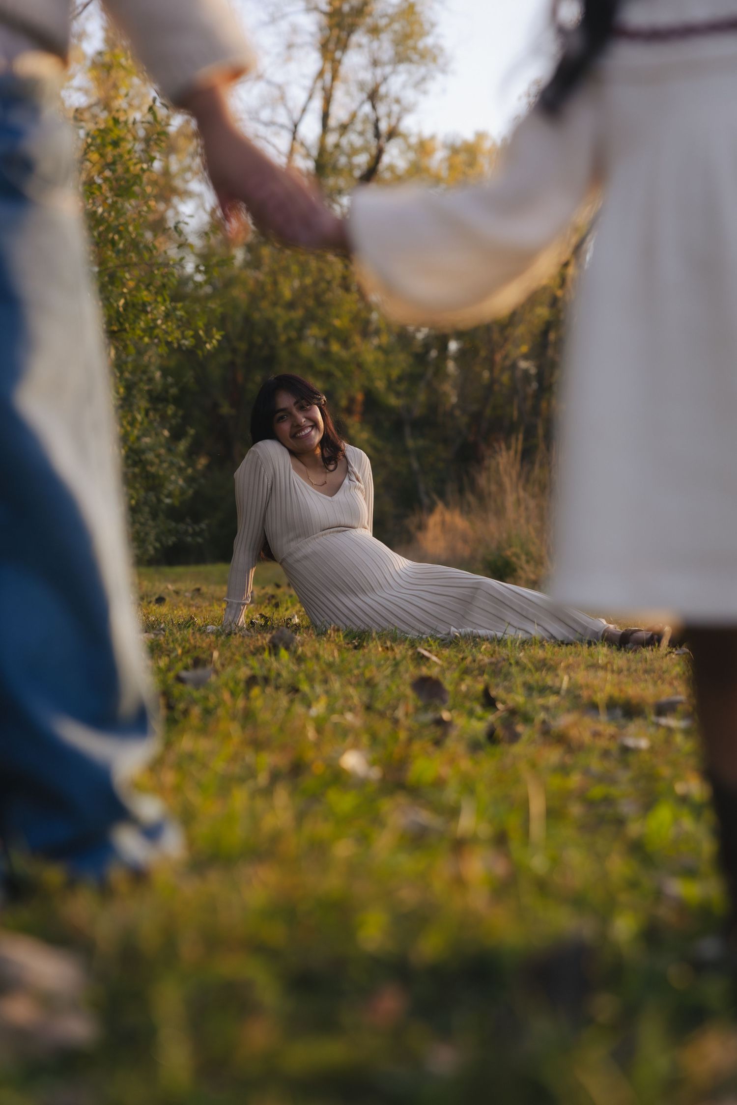 A person in a white sweater lies in a grassy field during golden hour as autumn leaves frame the peaceful scene.