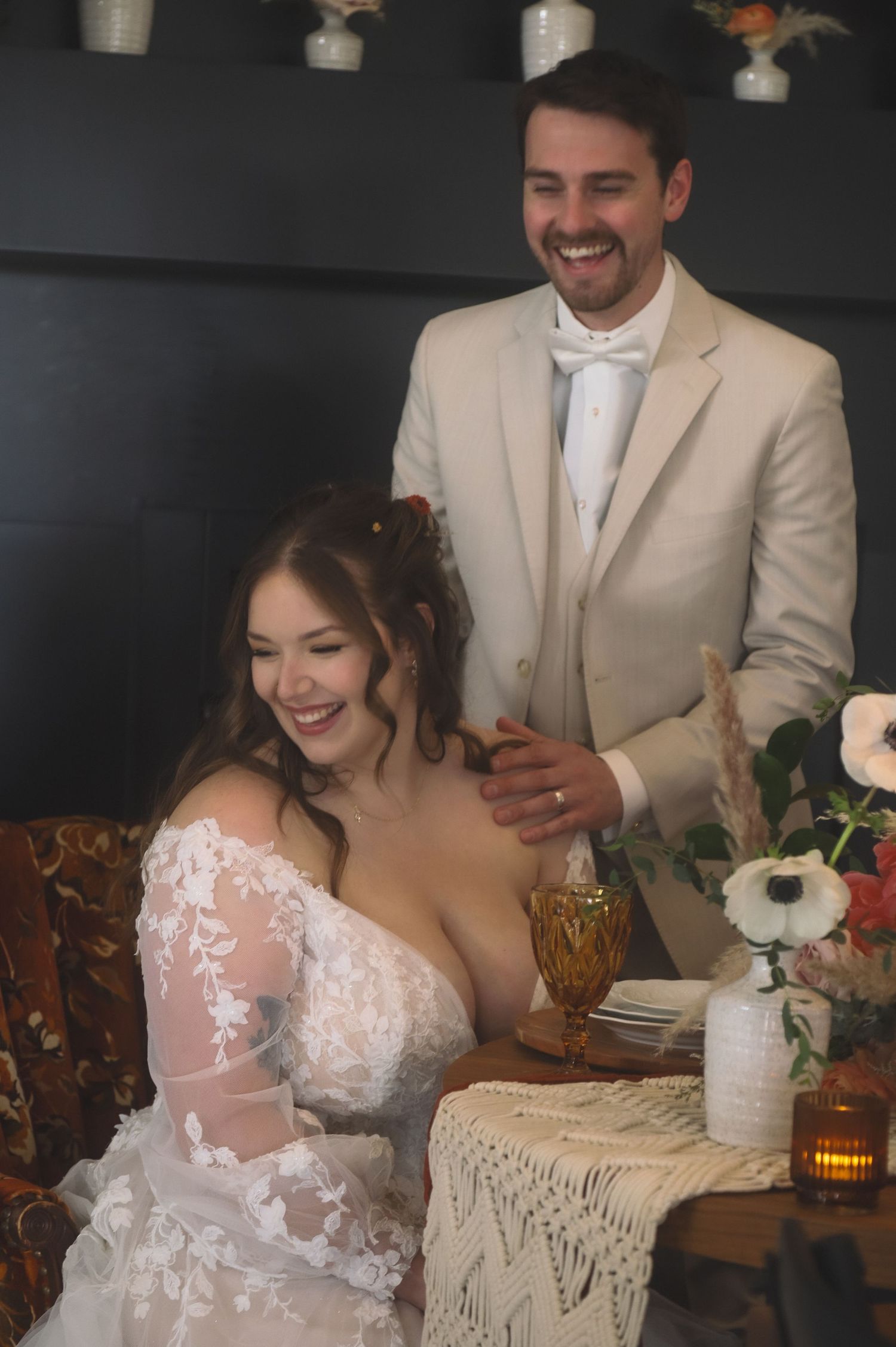 A couple shares a joyful moment at their wedding reception, with decor featuring a lace tablecloth and floral arrangements.