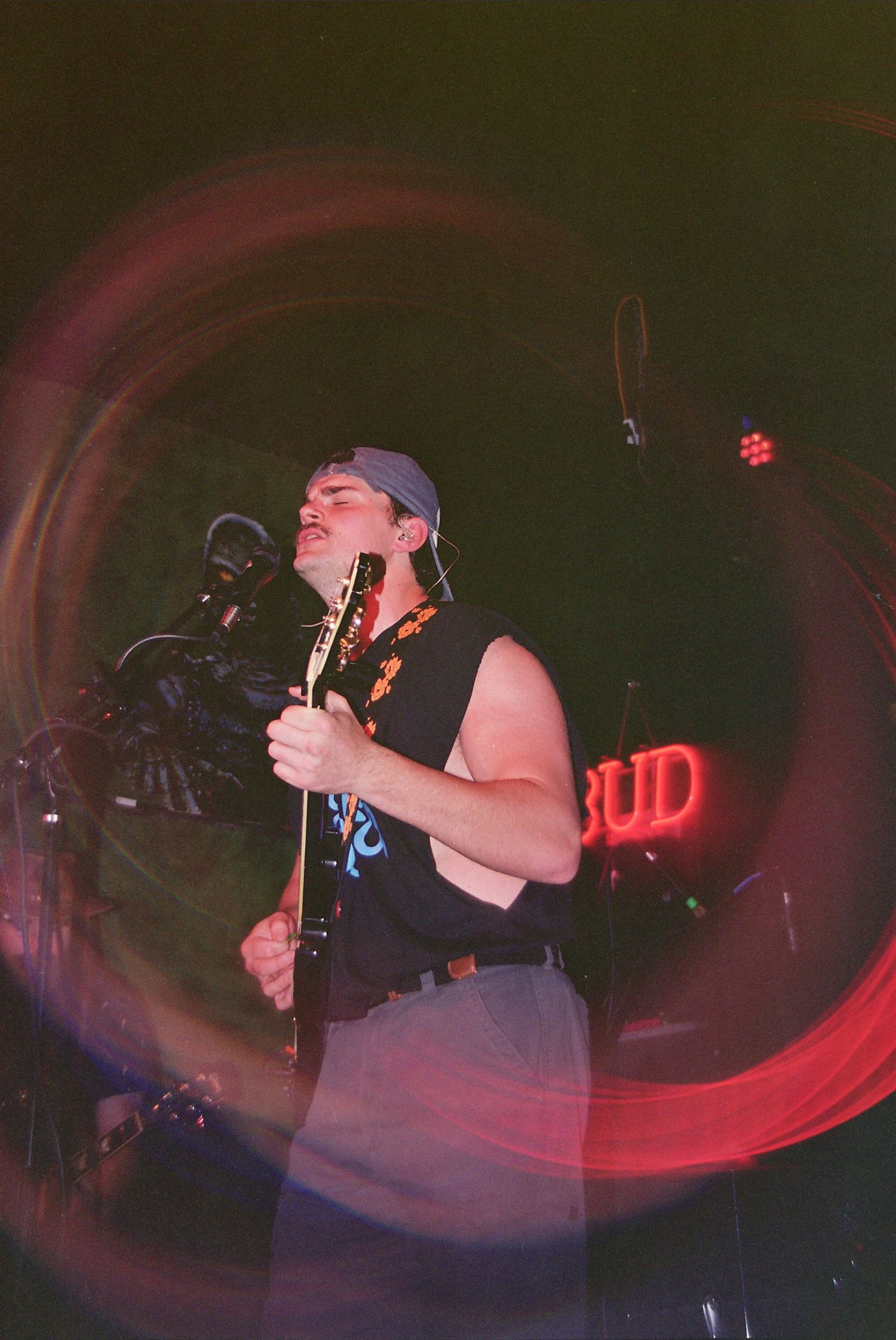 Musician performs on stage with guitar under dramatic red lighting near a Budweiser sign.