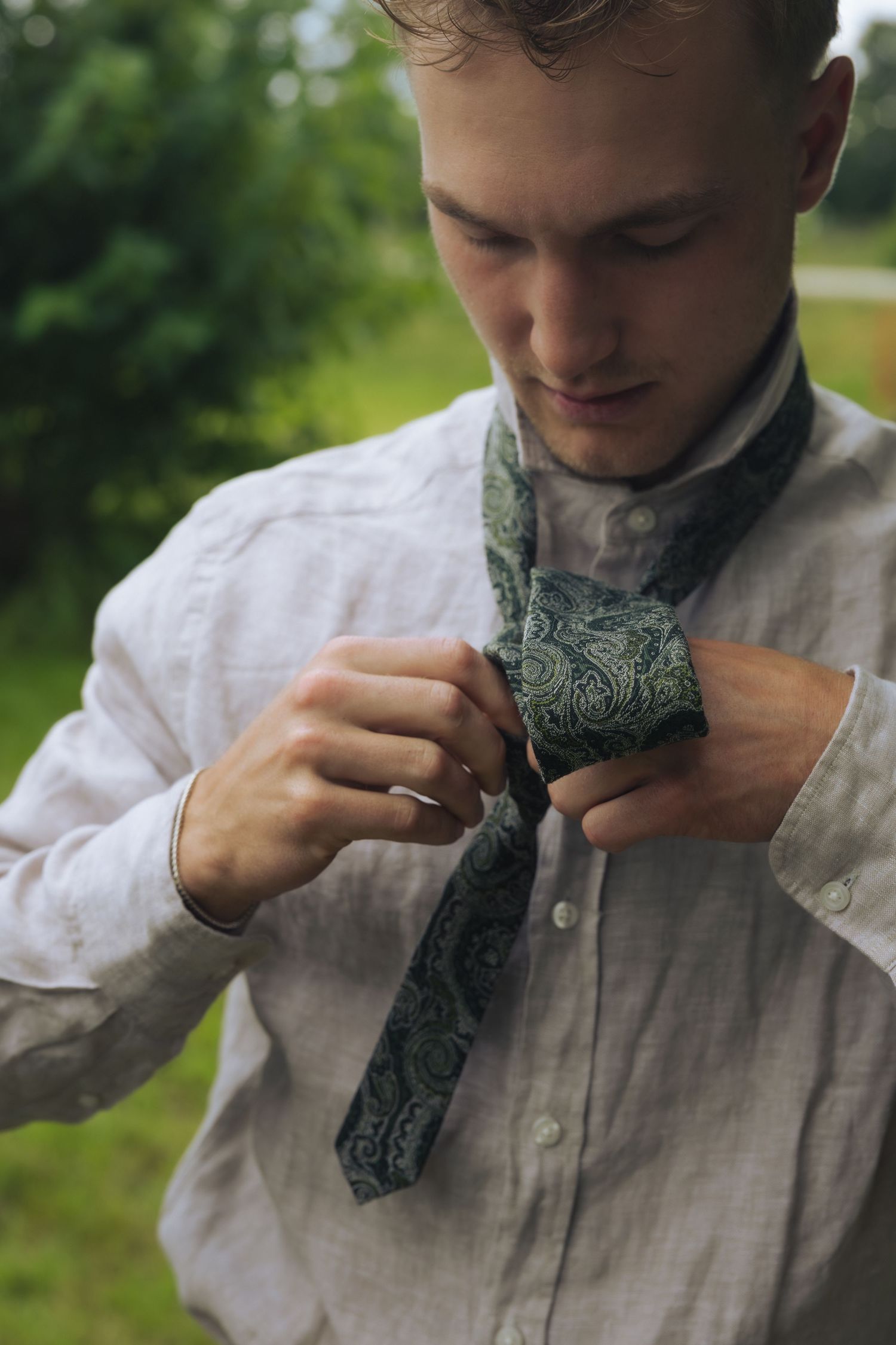 A person wearing a white button-down shirt adjusts a green patterned bowtie in a sequence of images.