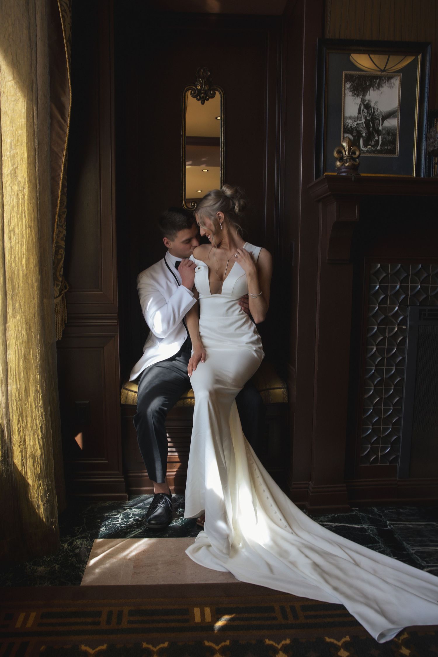 Couple in formal attire share an intimate moment in an elegant dark wood-paneled room with dramatic lighting.