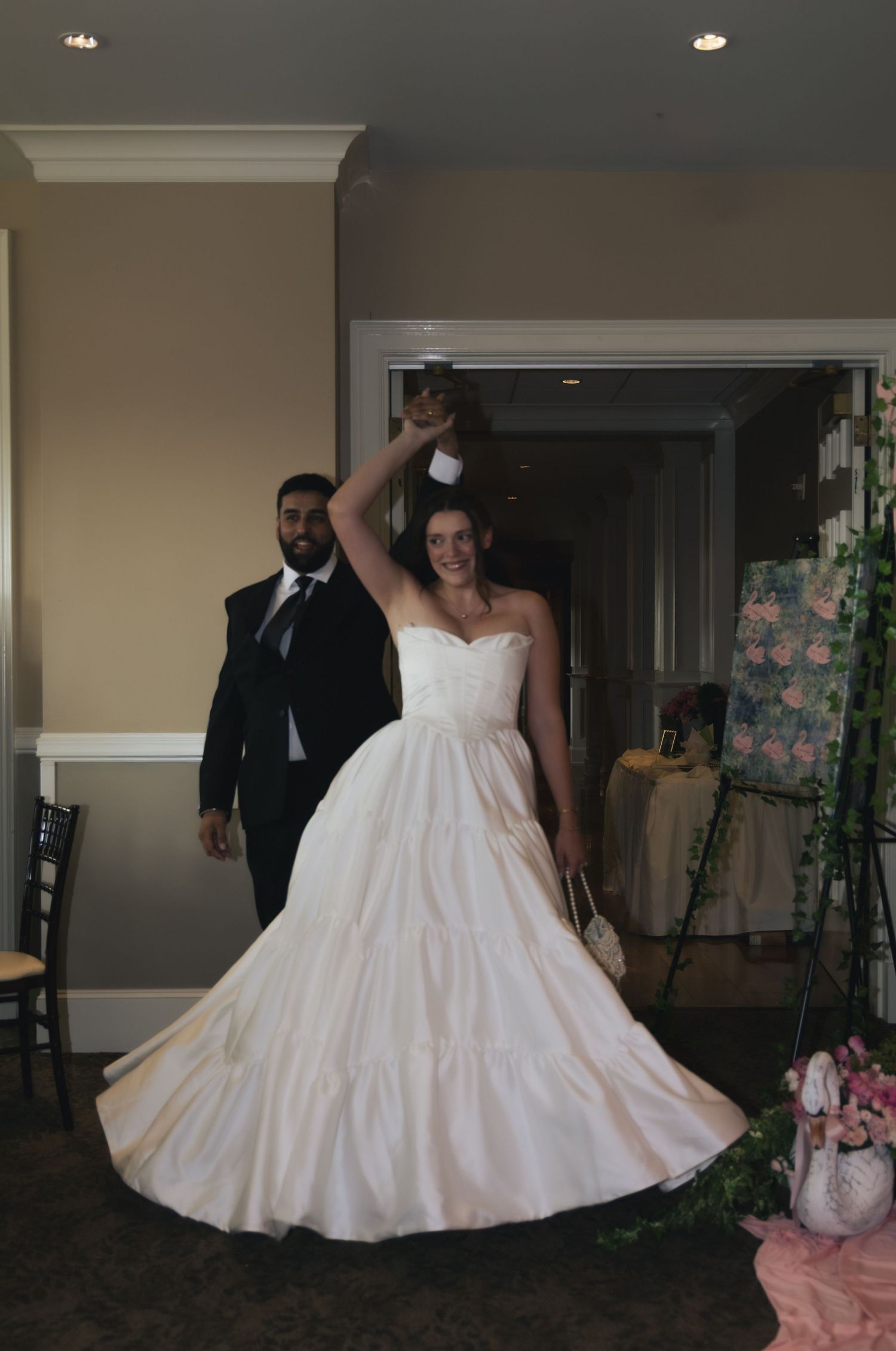 Bride in strapless ball gown twirls as groom in black suit leads grand entrance at wedding reception.