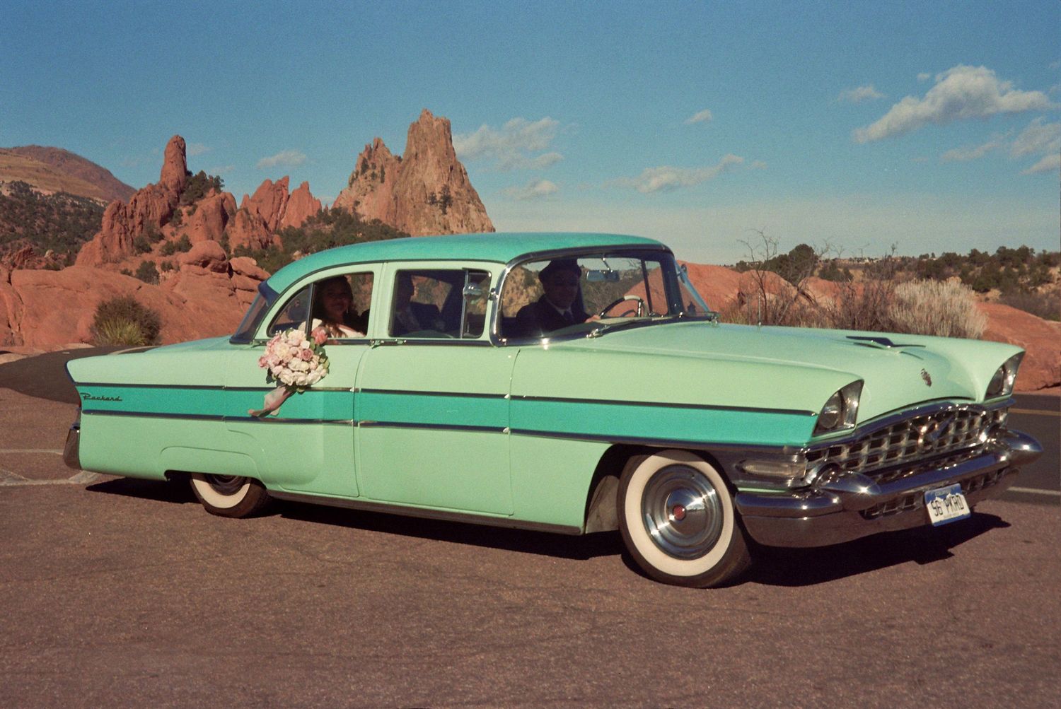 Vintage mint green 1950s classic car parked near red rock formations under a blue sky.