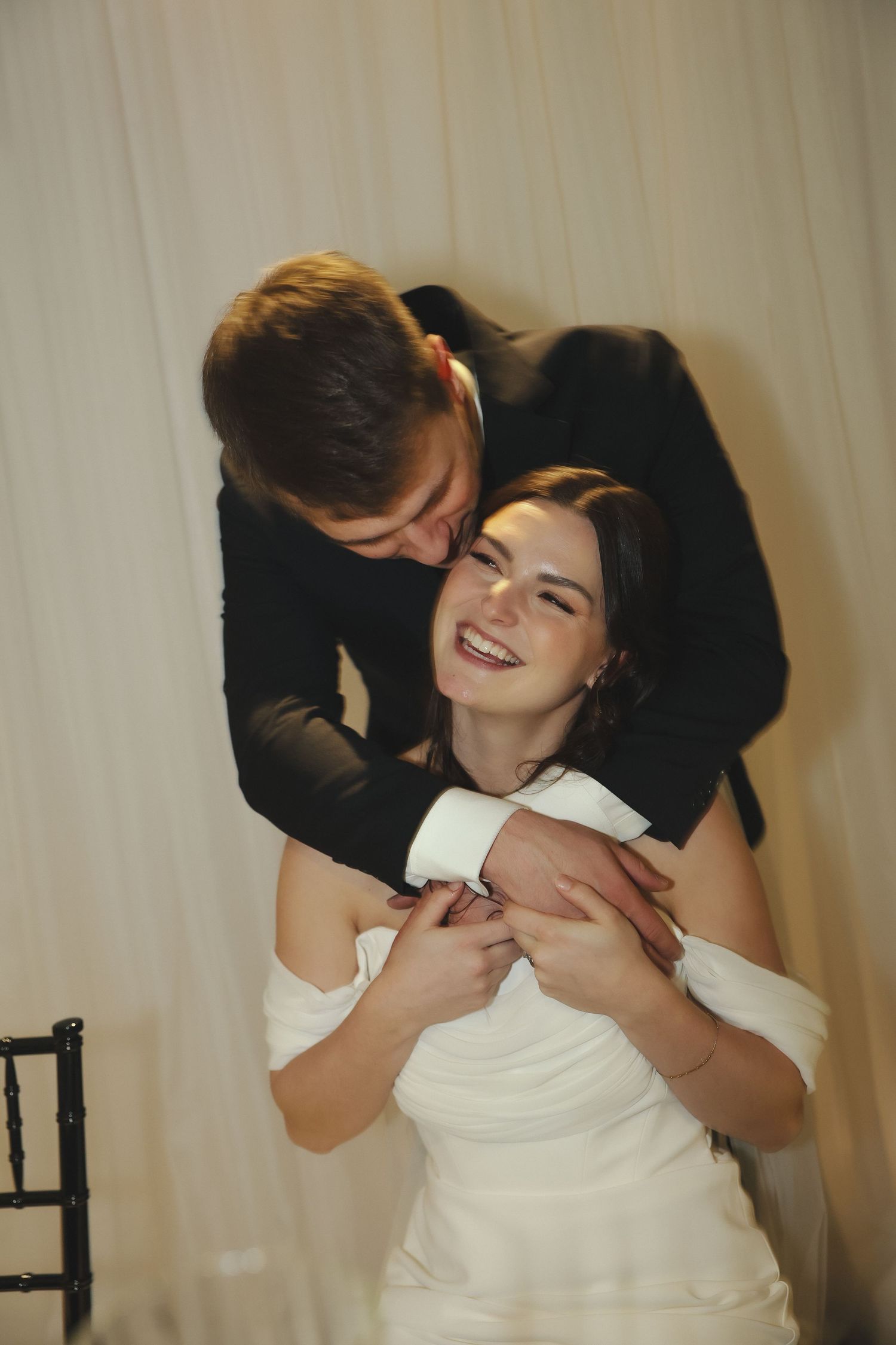 Wedding couple shares joyful embrace during intimate moment against neutral background.