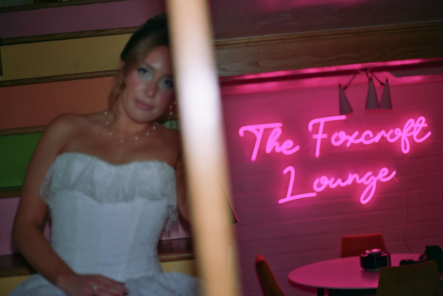 A dimly lit nightclub interior with pink neon signs and bar seating visible in the background.