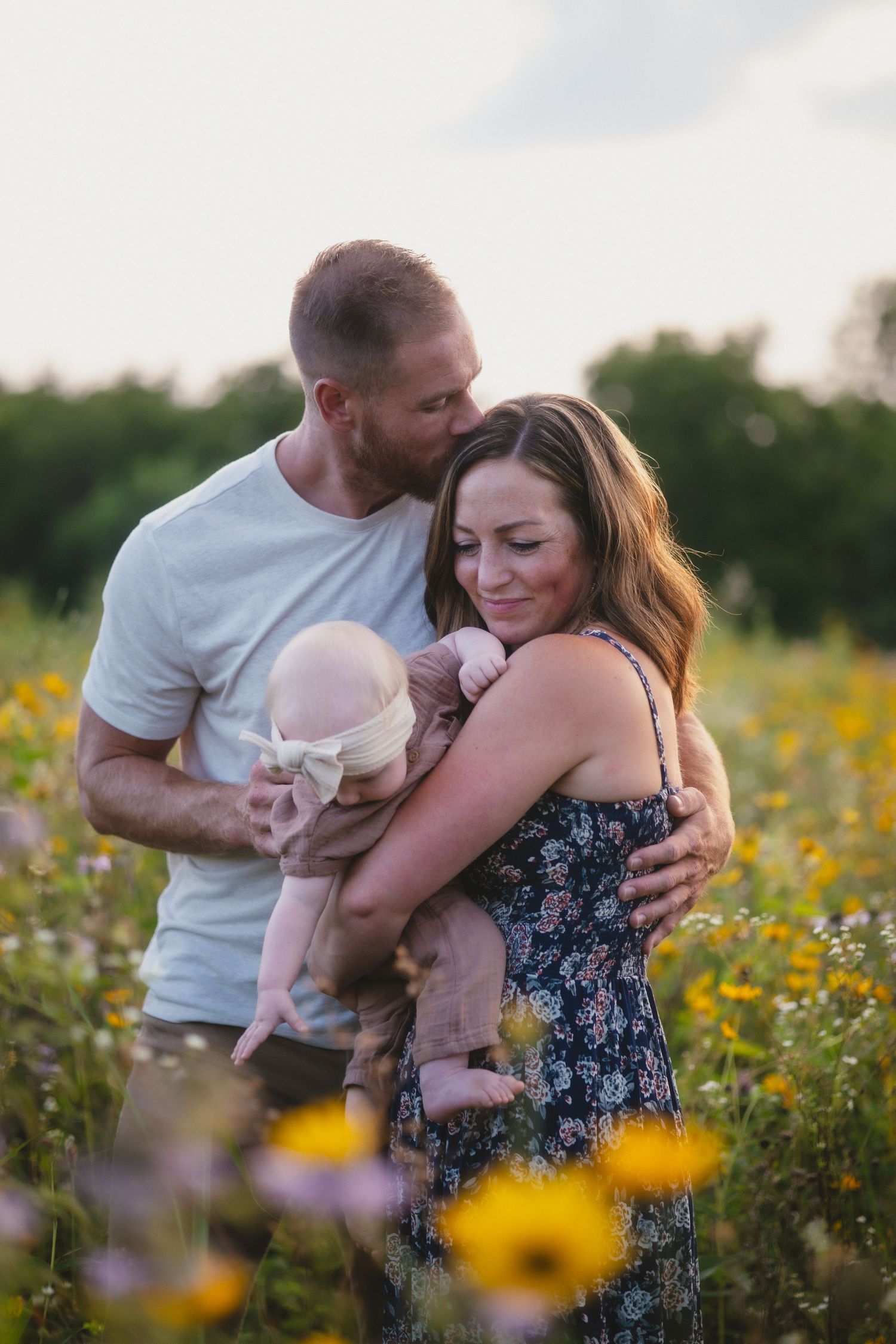 A couple embraces while standing in a field of yellow wildflowers during golden hour in summer.