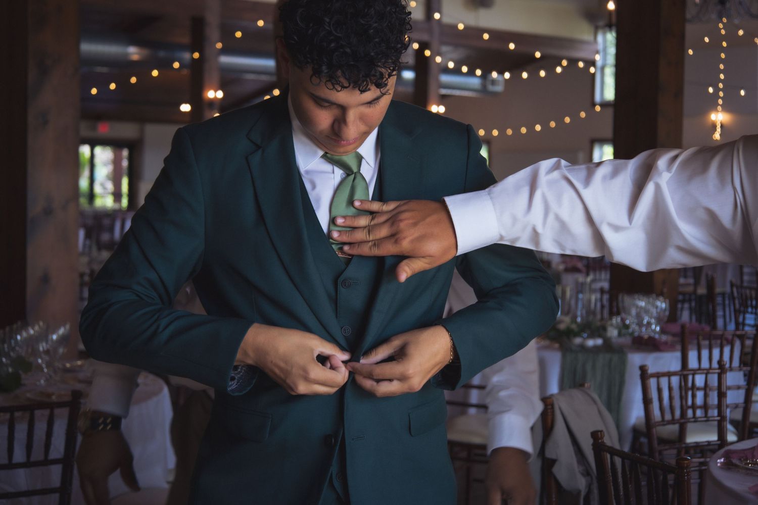 A formal suit adjustment being made in a room with twinkling lights.
