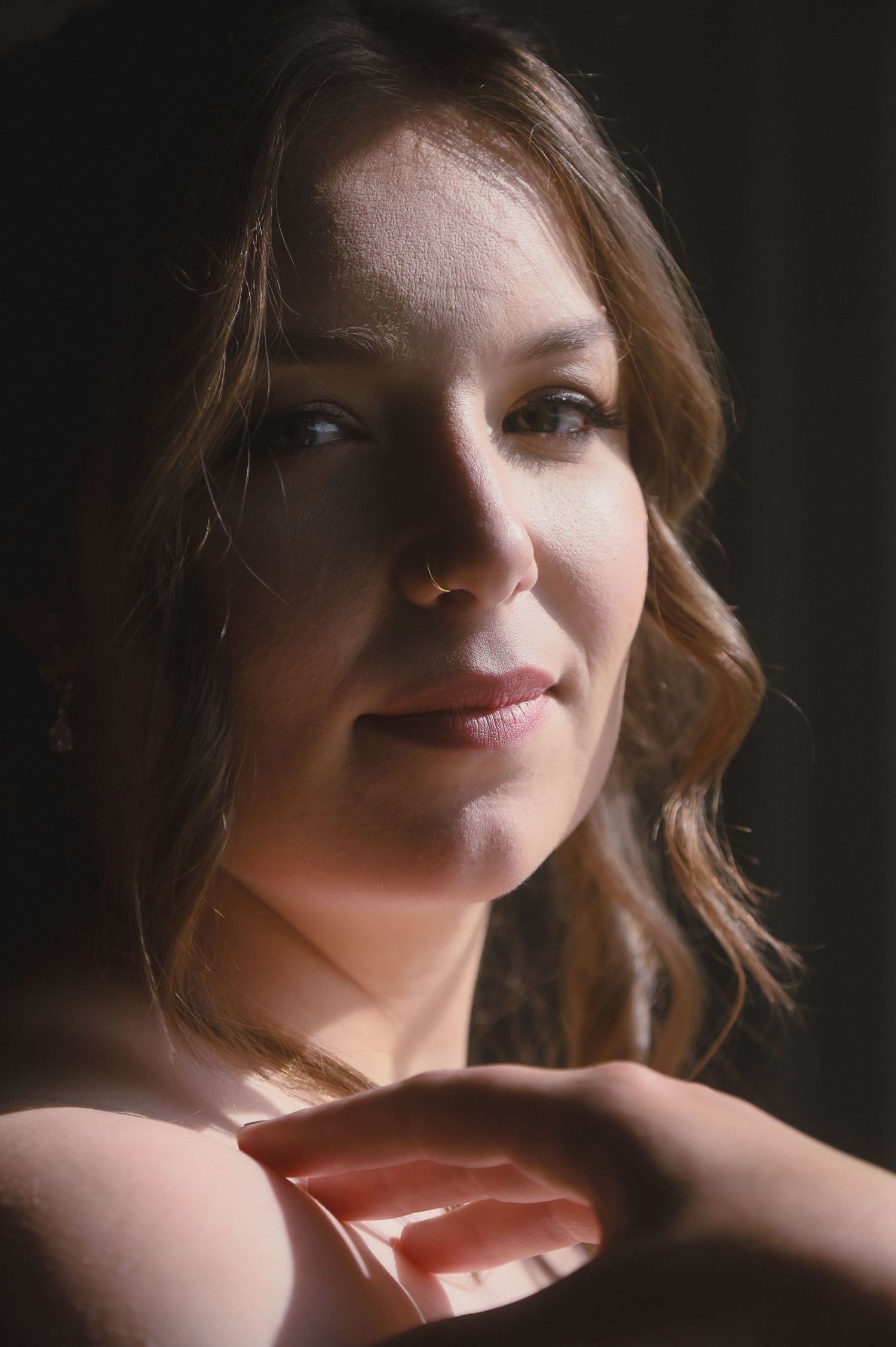 Artistic portrait with soft lighting and warm tones shows a gentle smile against a dark background.