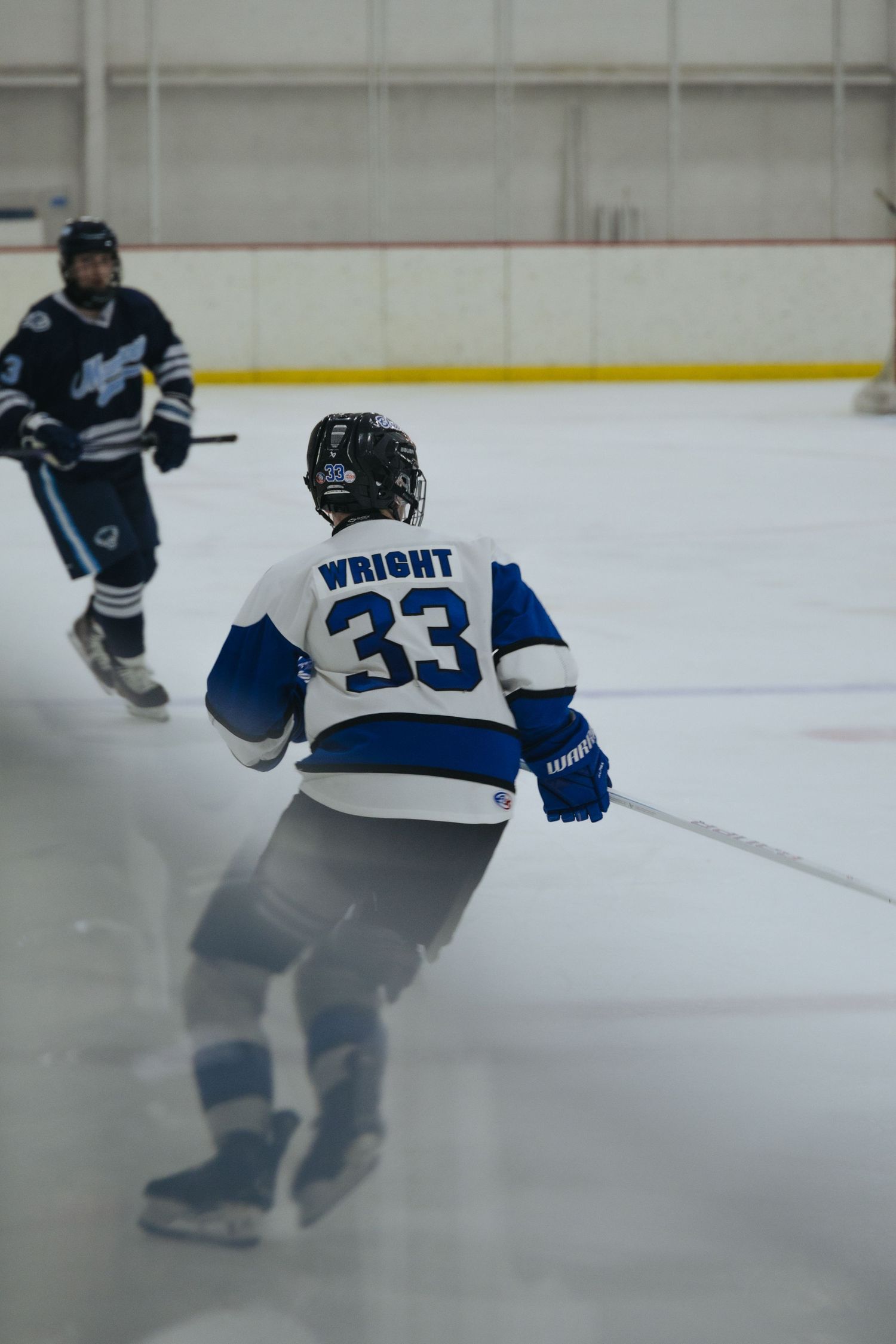 Hockey player in blue and white jersey number 33 performs a skating maneuver on ice during a game.