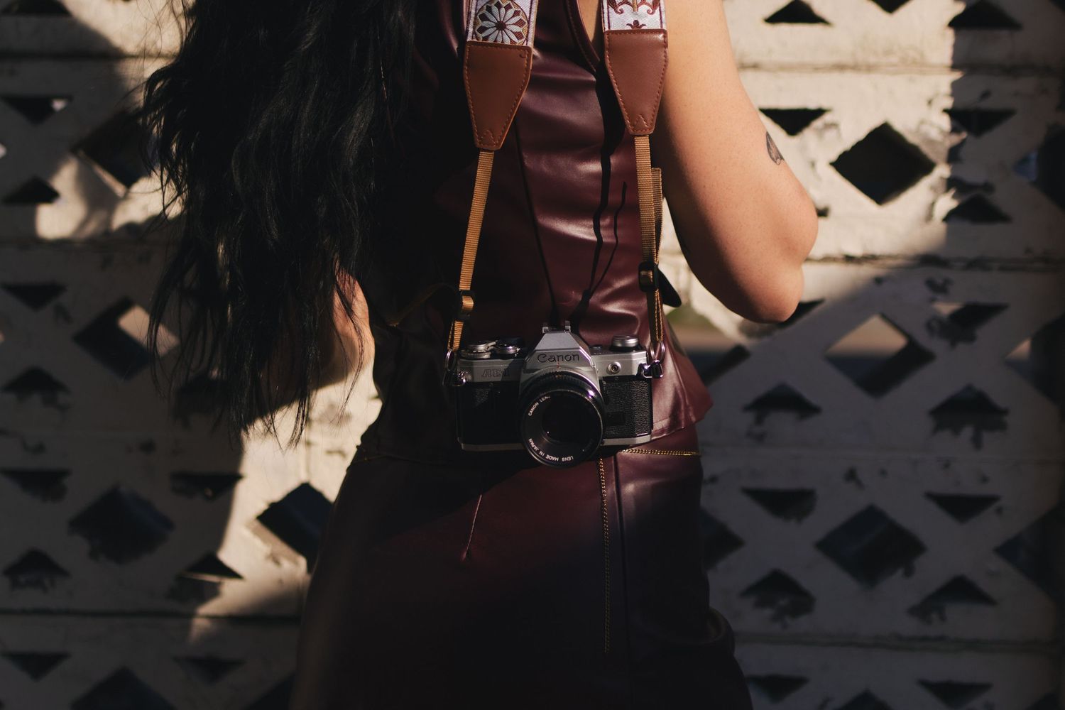 Woman with long dark hair wearing a burgundy leather outfit with a vintage film camera on a yellow strap.