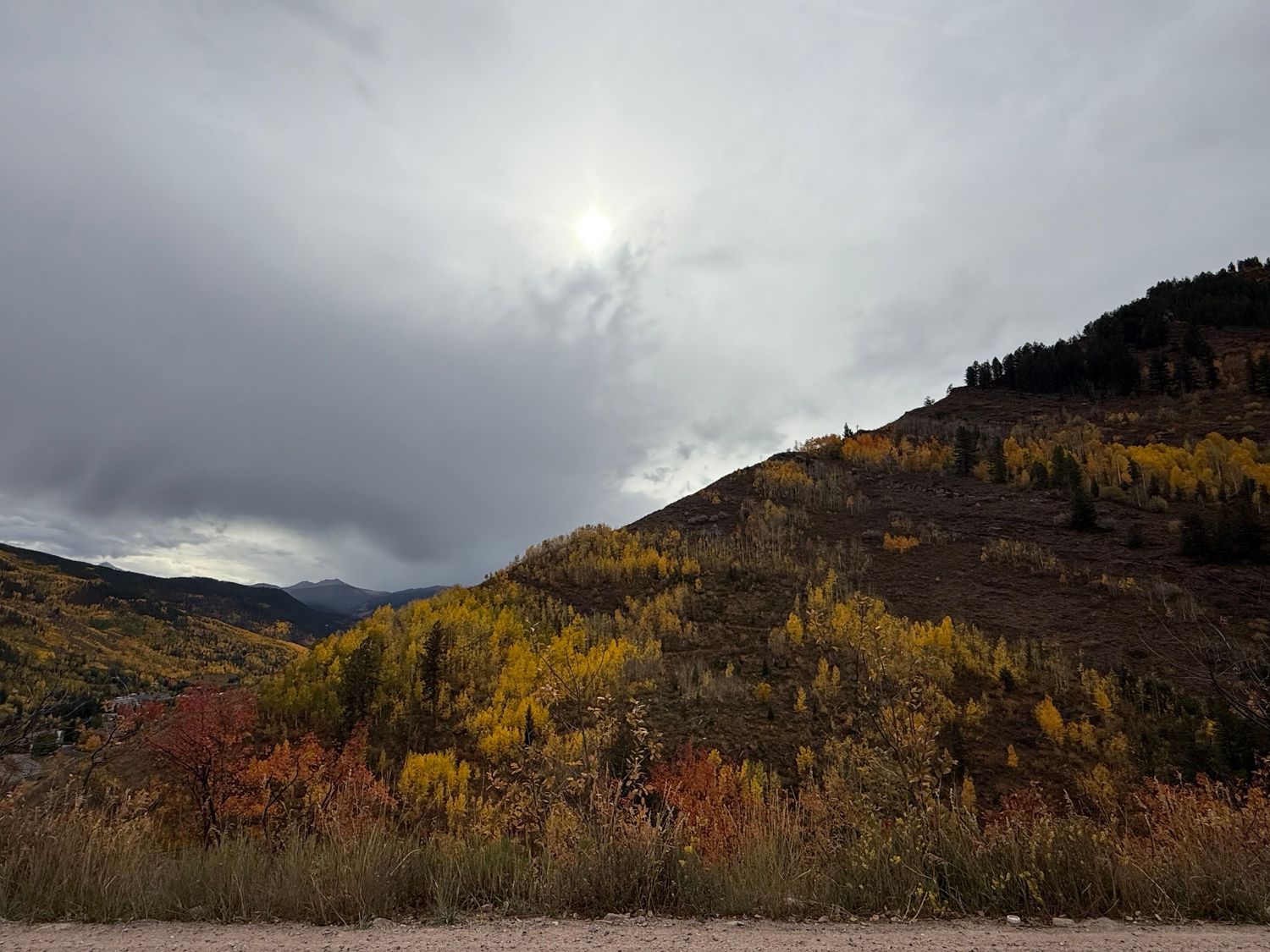 A panoramic mountain landscape with autumn foliage and dramatic cloudy skies over a scenic valley.