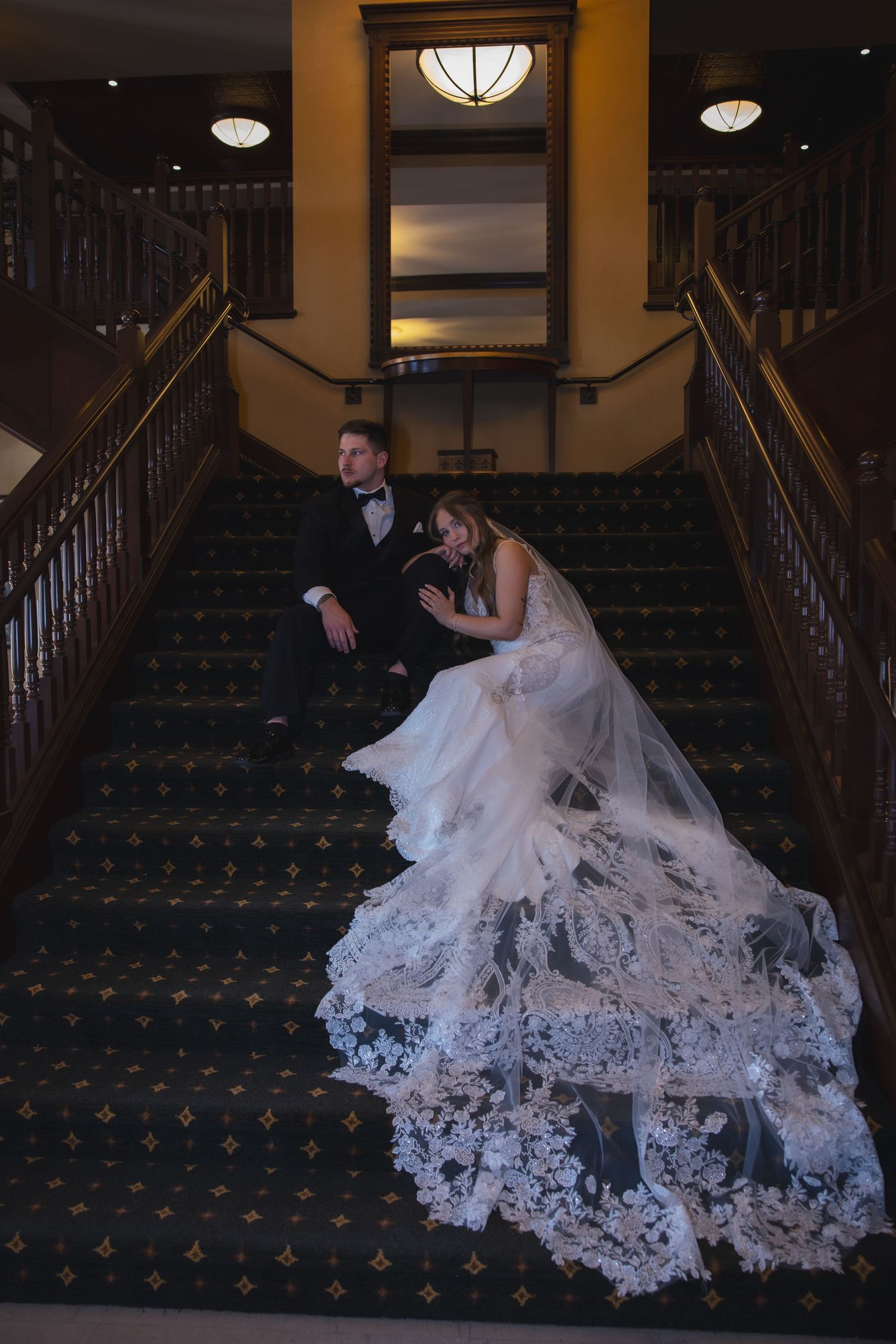 A romantic wedding photo on a grand carpeted staircase with an ornate lace dress trailing down the steps.