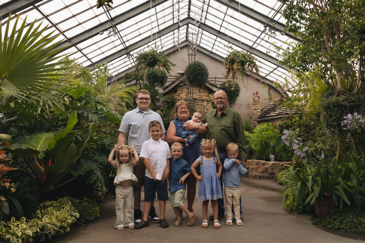 Family portrait in a lush greenhouse conservatory surrounded by tropical plants and glass ceiling.