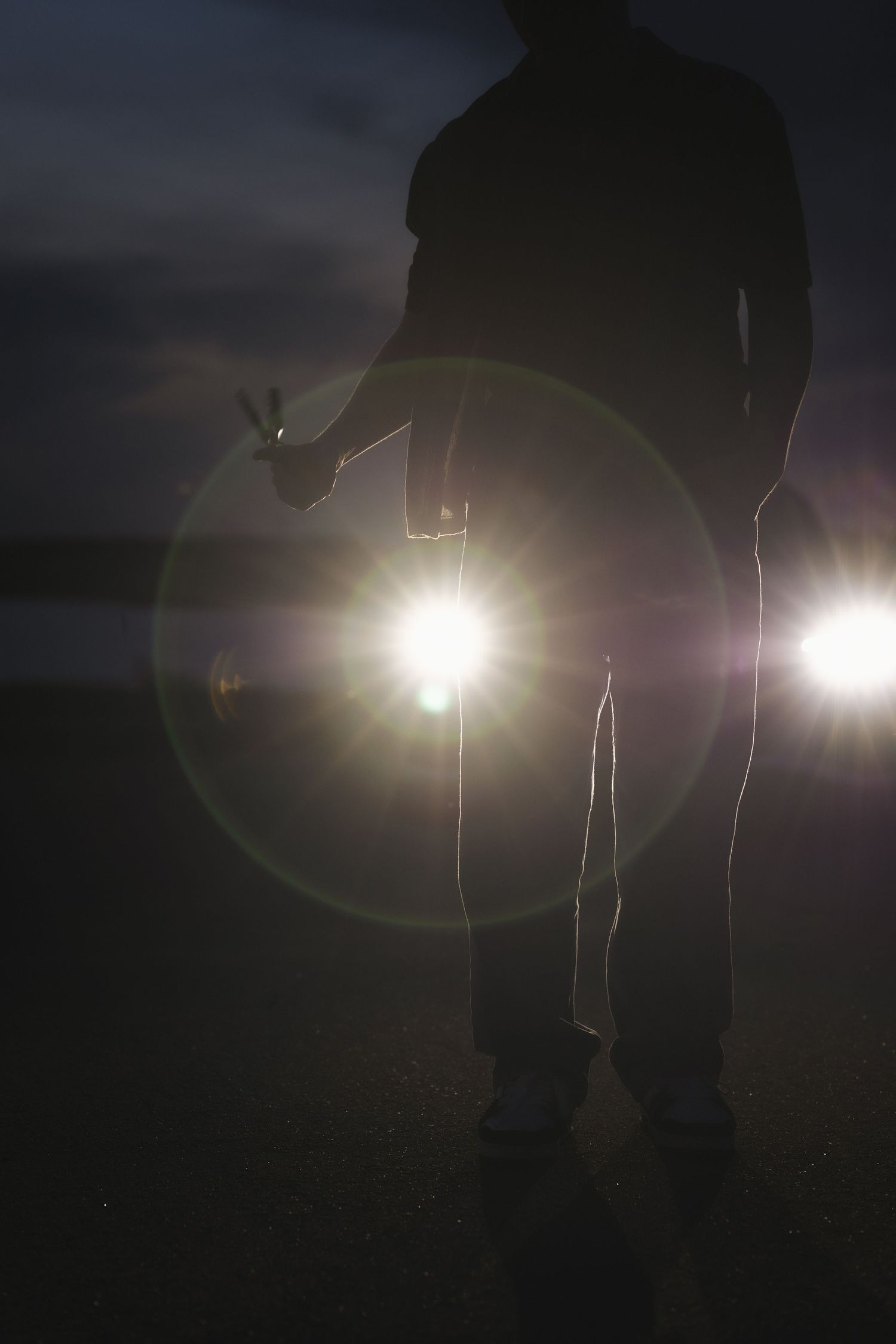 Silhouette of a person standing in front of bright car headlights at night with lens flare effect.