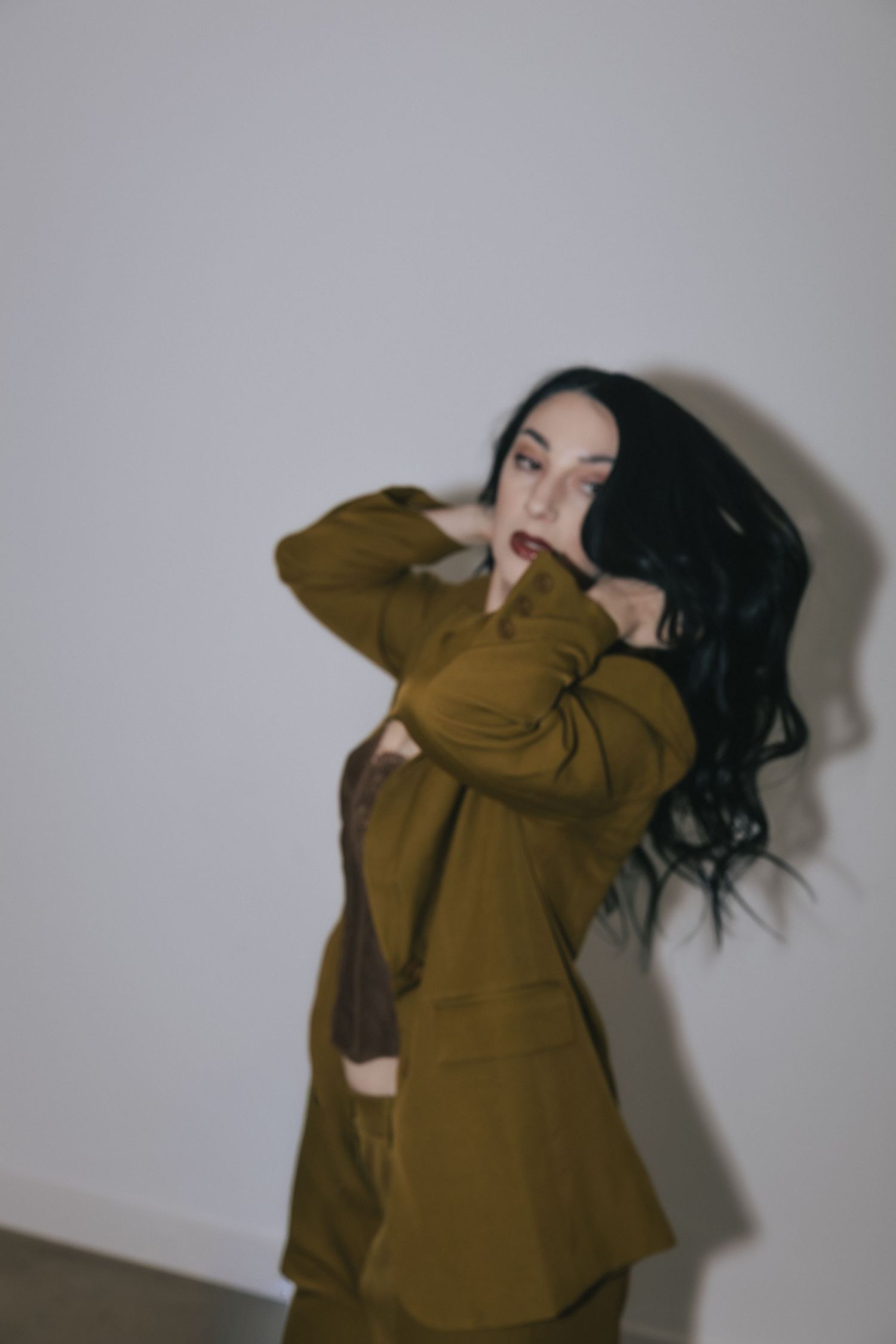 Person in brown oversized sweater moves dynamically against white wall in artistic photo sequence.
